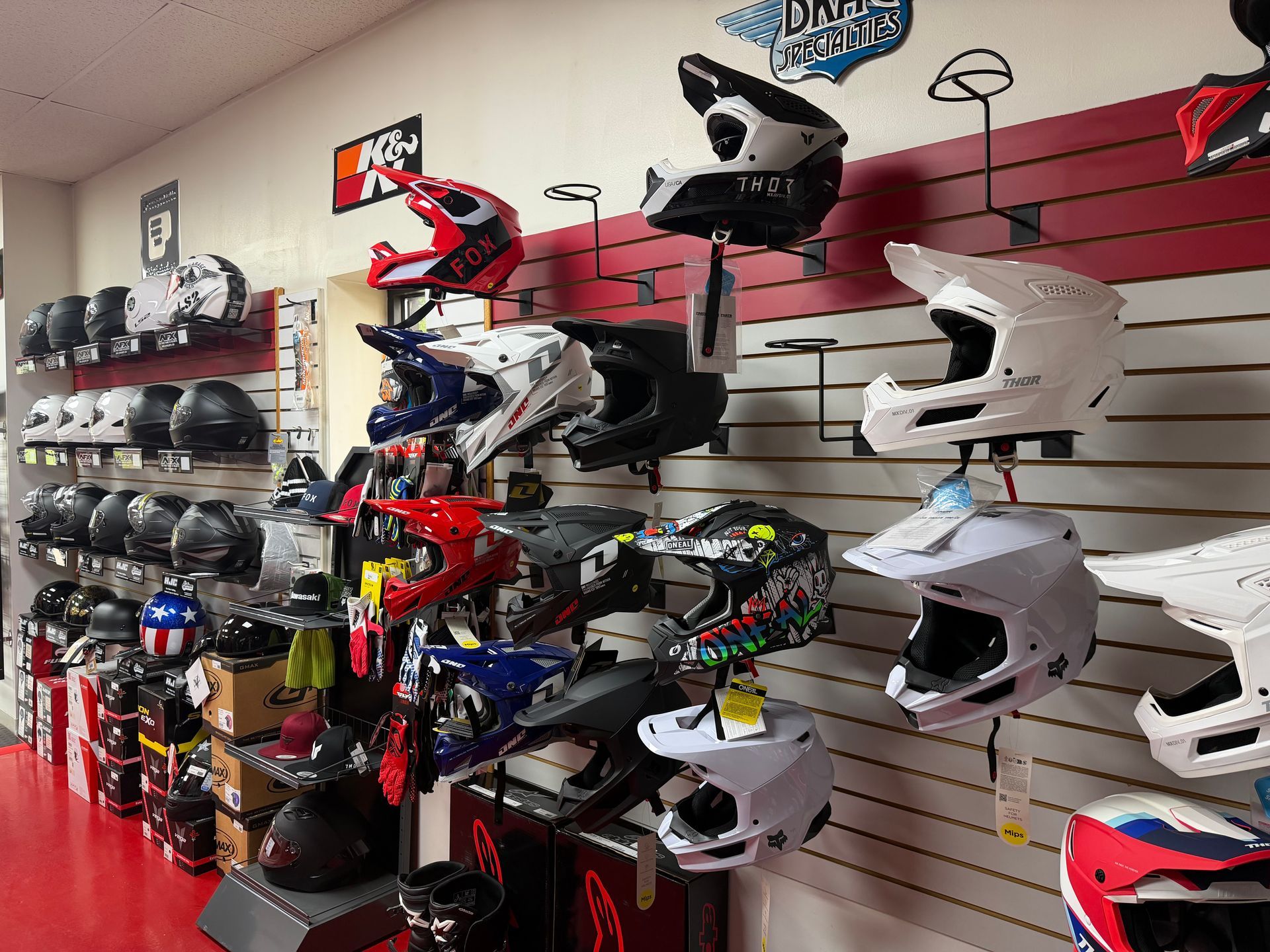Wall of motorcycle helmets displayed on slatwall shelves in a store, with various colors and styles.