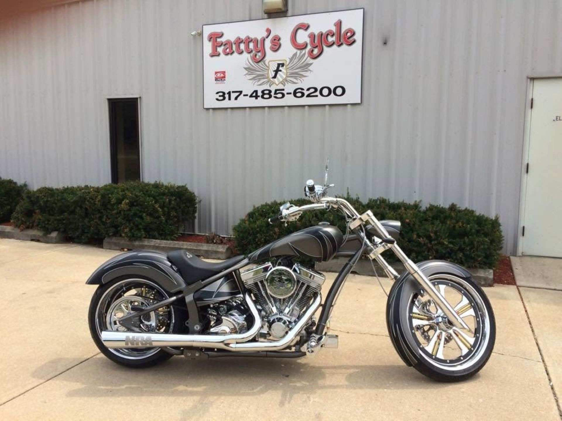 Custom motorcycle parked outside a motorcycle shop building.