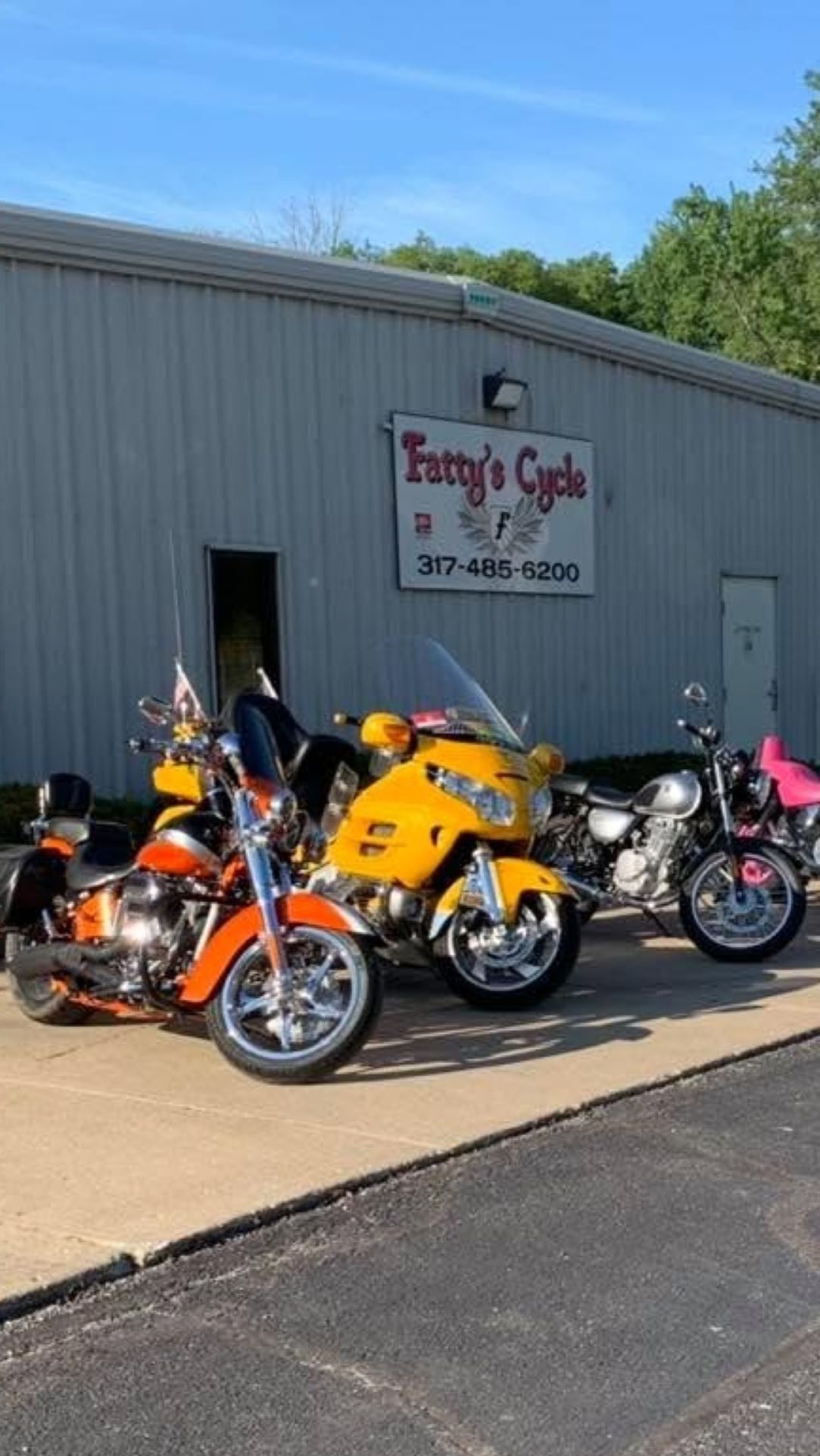 Three motorcycles parked outside Funny’s Cycle shop on a sunny day