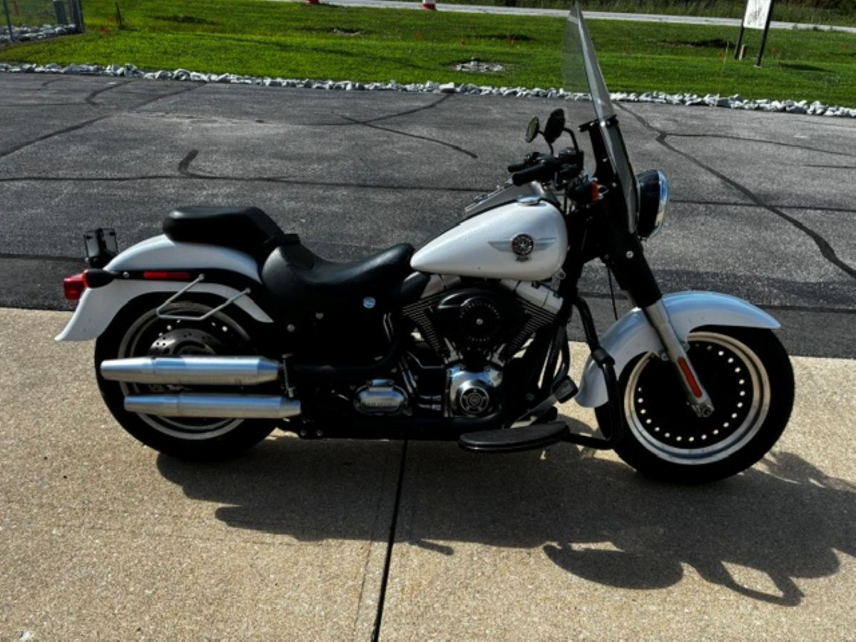 White and black cruiser motorcycle parked on cracked pavement near grass.
