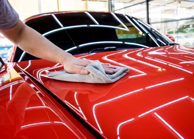 Person wiping a shiny red car with a gray cloth.