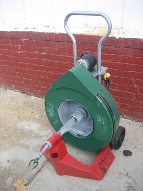 A green and red drain cleaner is sitting on the sidewalk