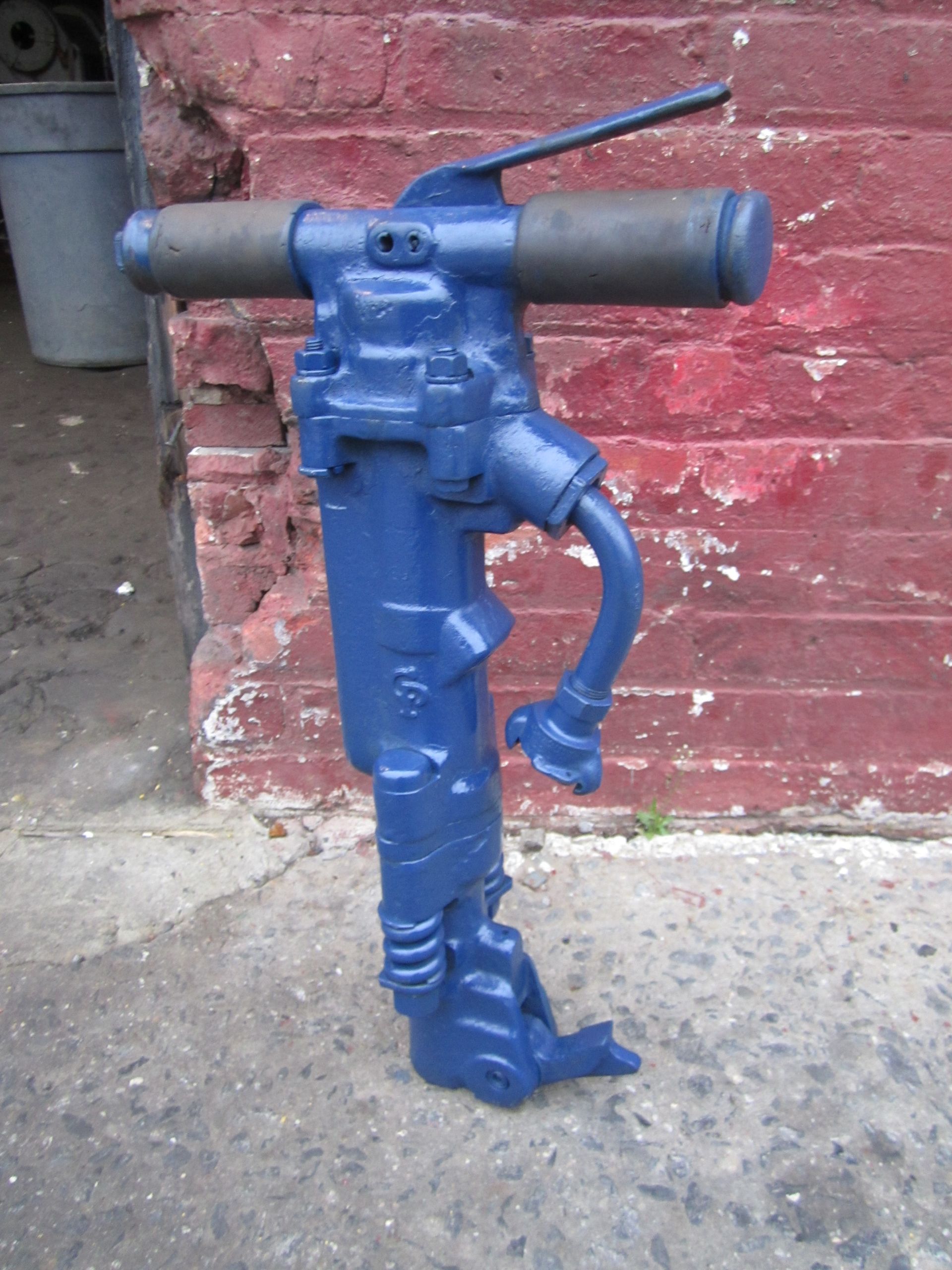 A blue drill is sitting in front of a red brick wall