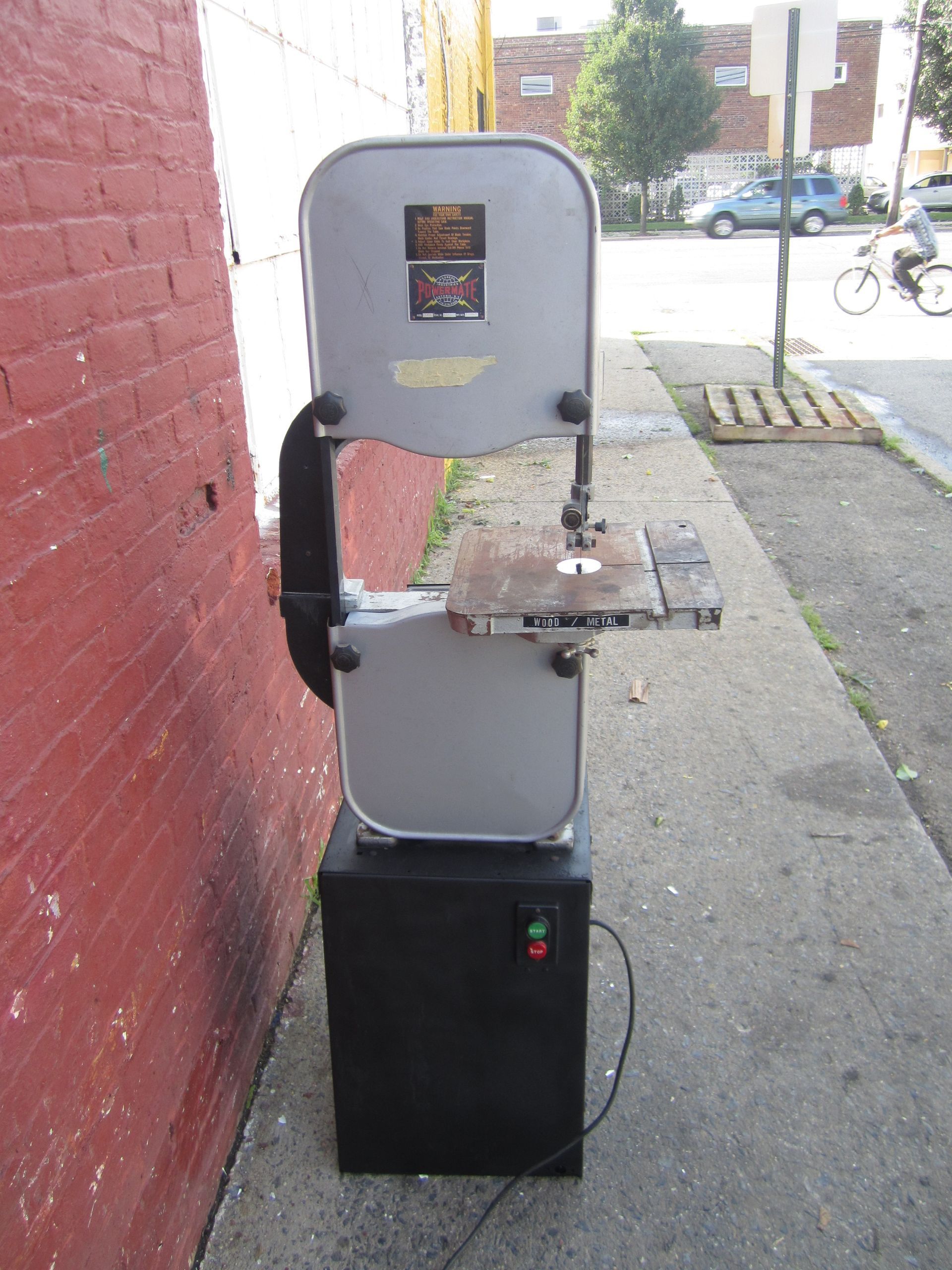 A band saw is sitting on a sidewalk next to a brick wall