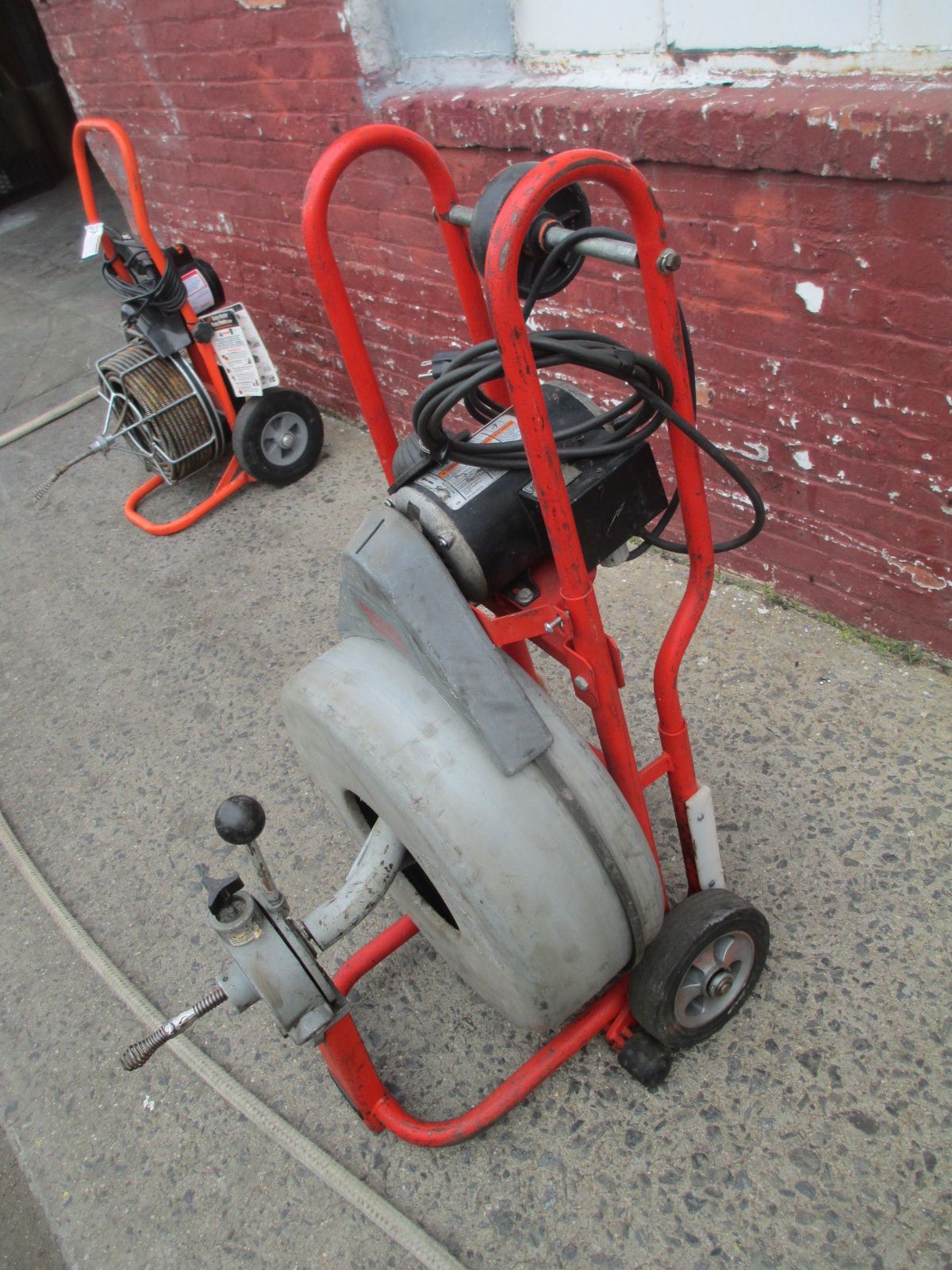 A drain cleaner is on a cart in front of a brick wall