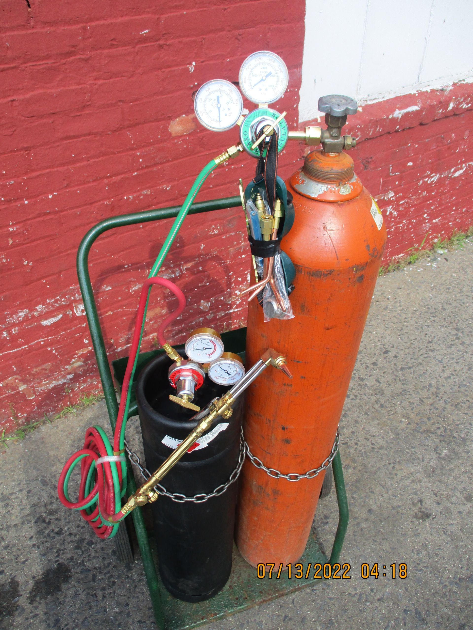 Two gas cylinders on a cart with a red brick wall in the background