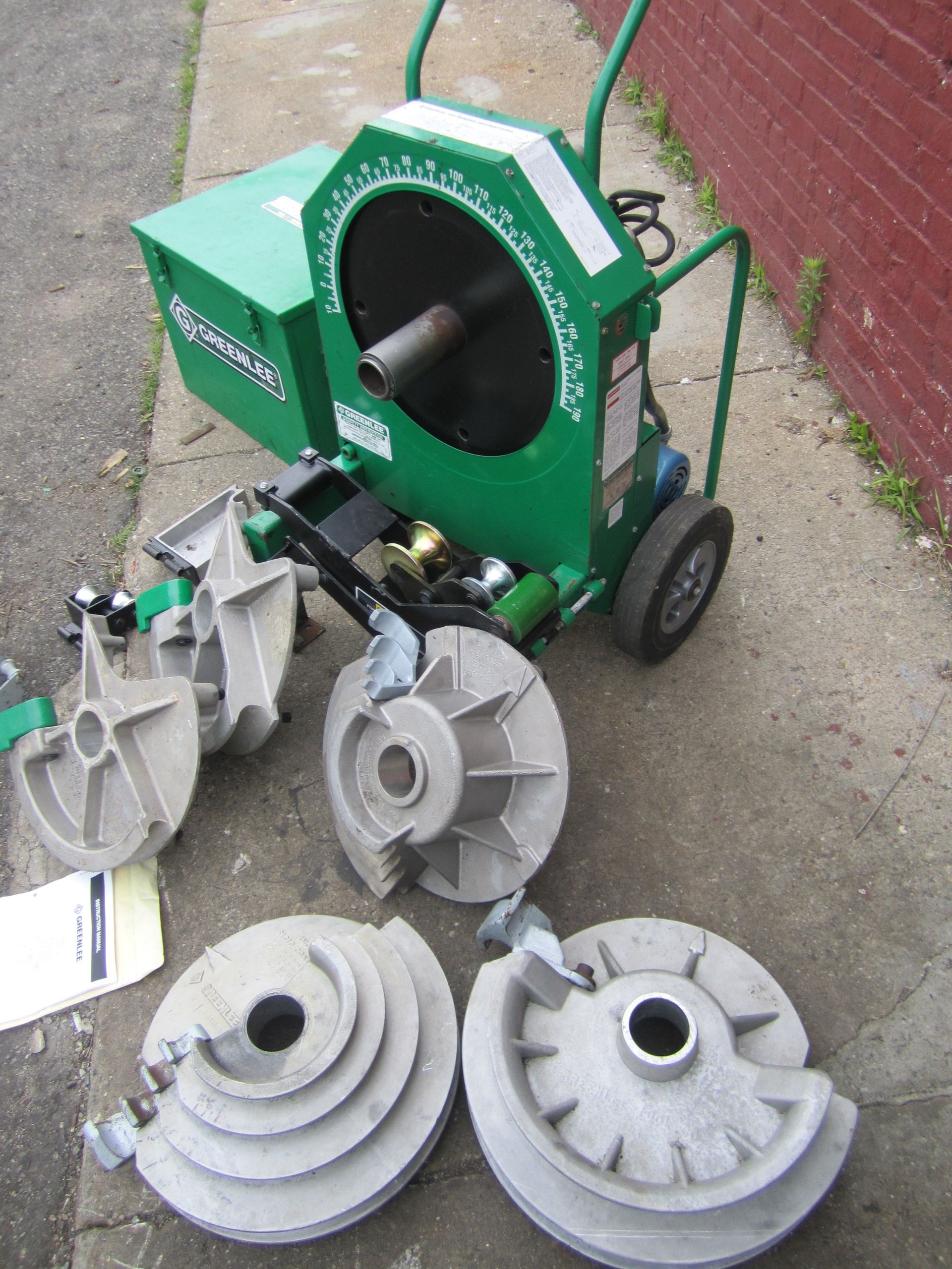 A green machine is sitting on a sidewalk next to a brick wall