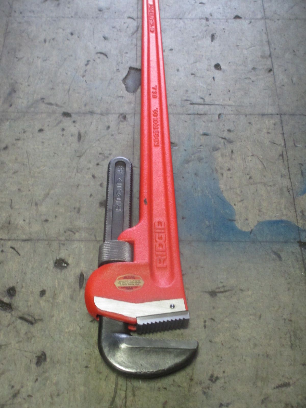 A red pipe wrench is sitting on a tiled floor
