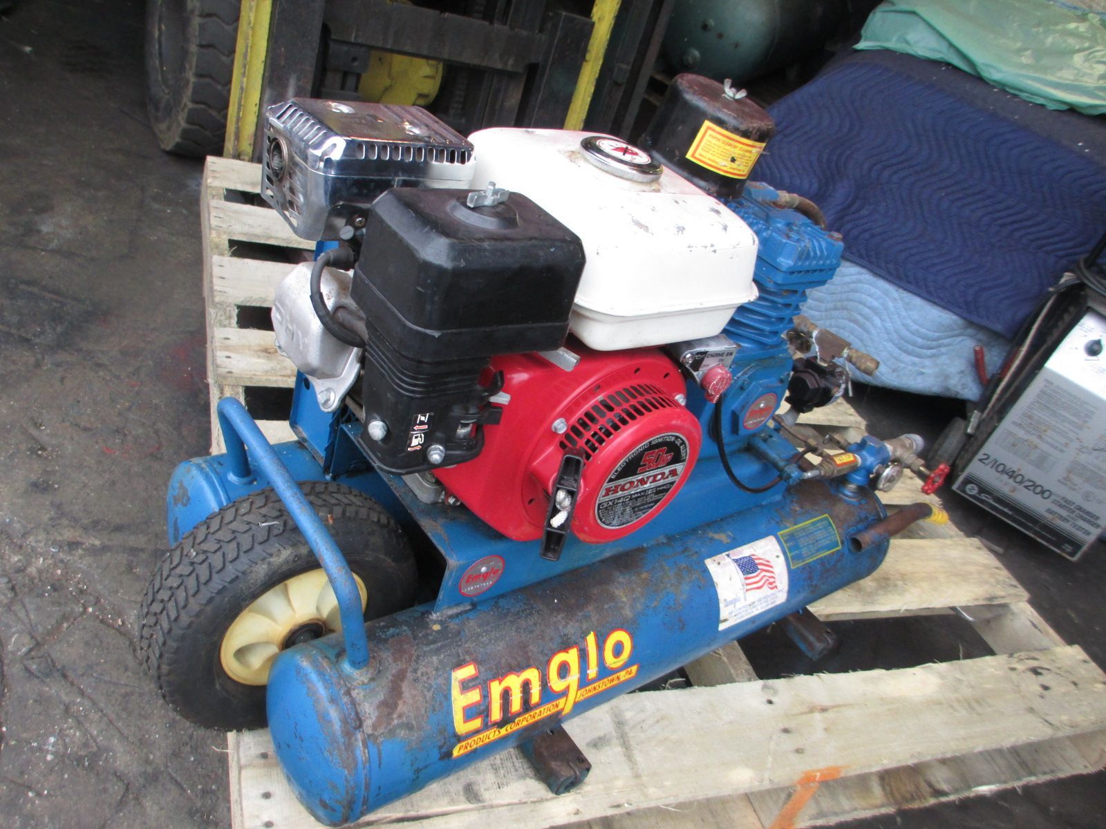 A blue air compressor with a red engine is sitting on a wooden pallet