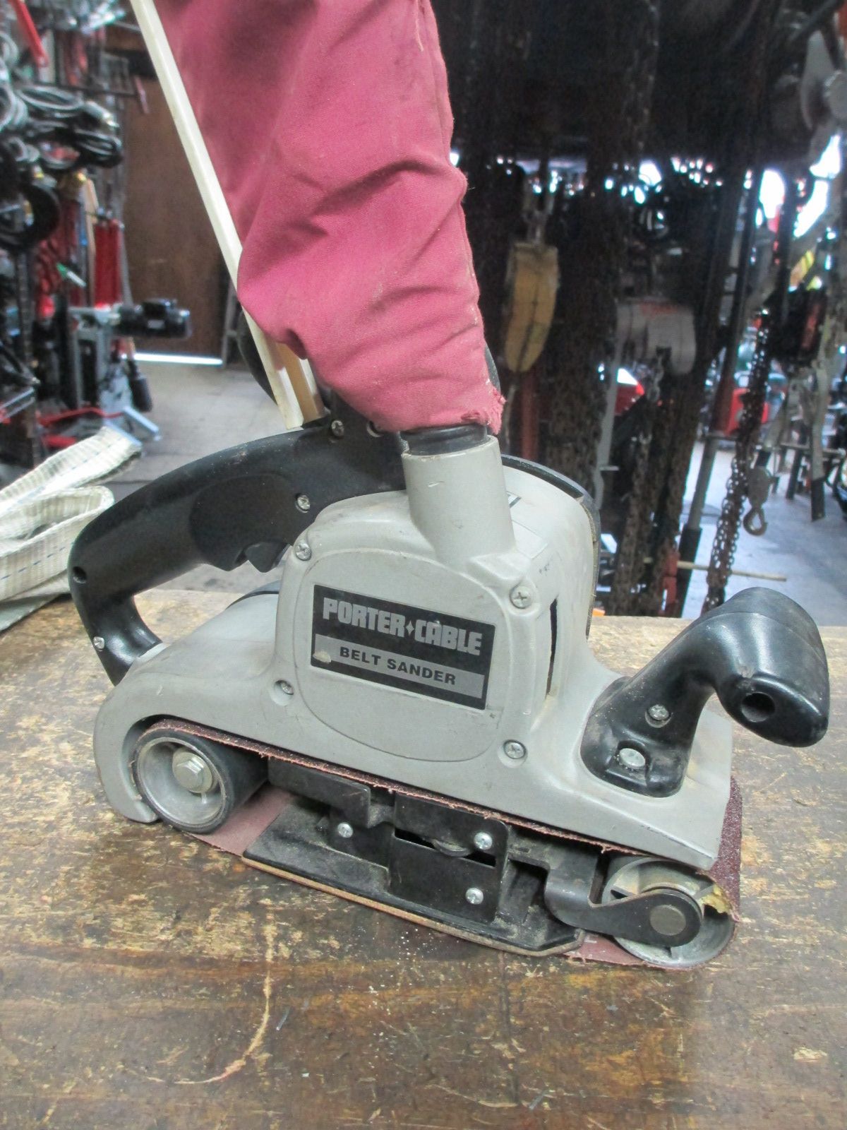 A person is using a belt sander on a wooden table.