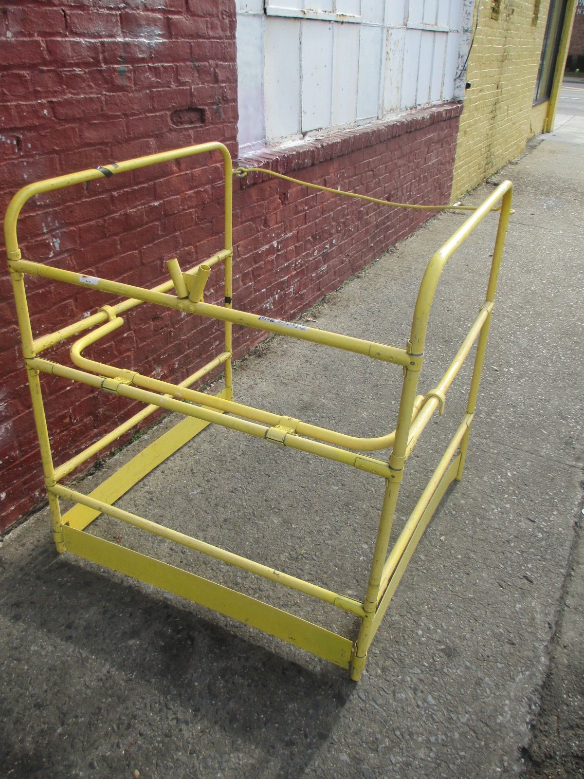A yellow metal railing is sitting on the sidewalk in front of a brick wall.