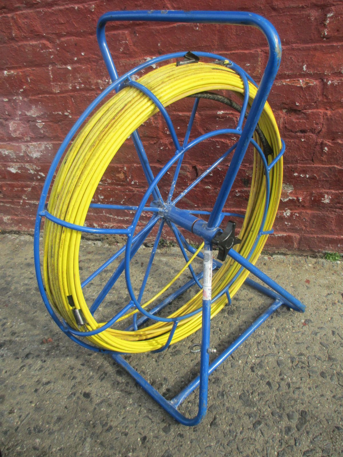 A blue and yellow hose reel is sitting in front of a brick wall