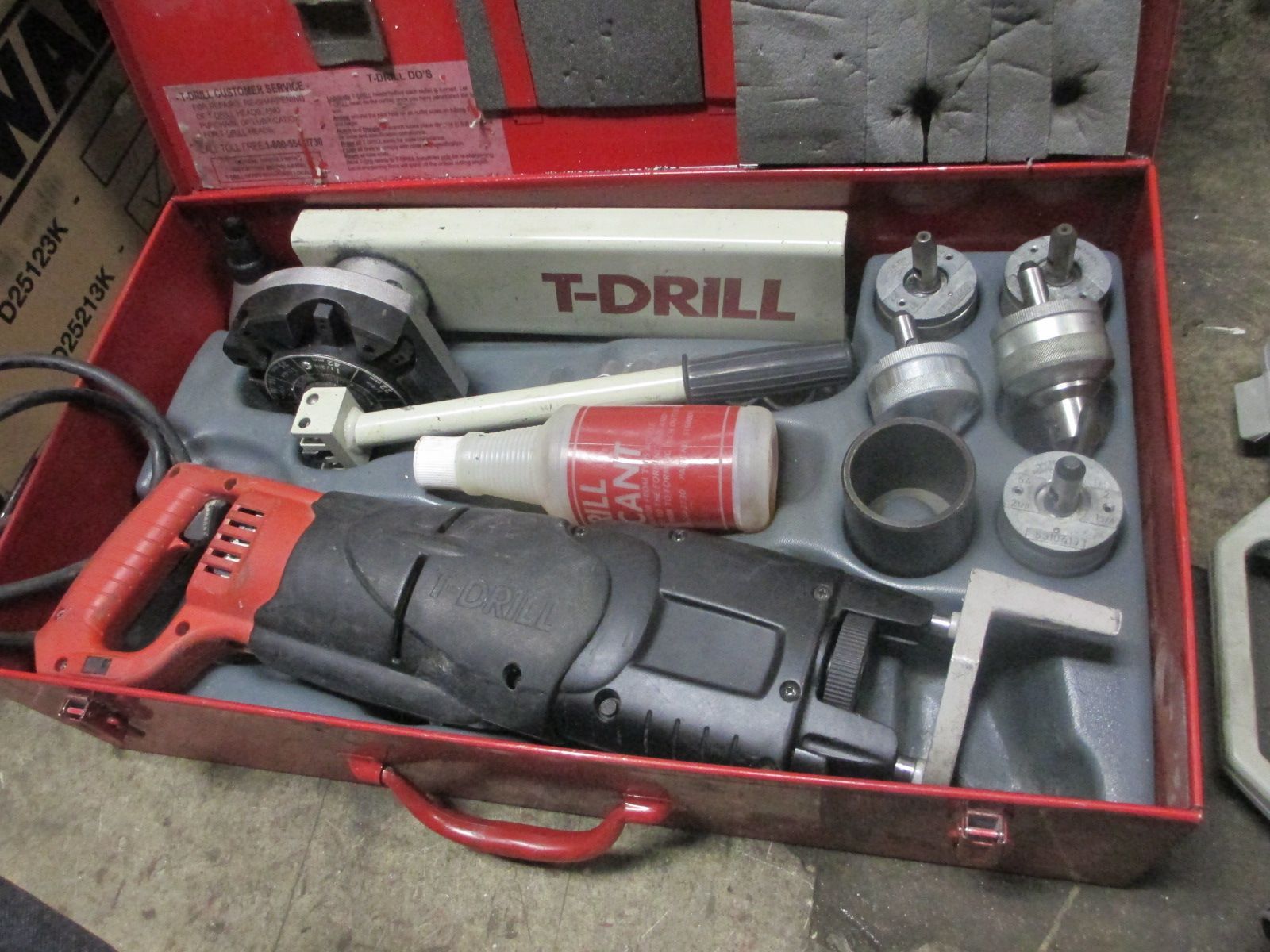A t-drill is sitting in a red case filled with tools
