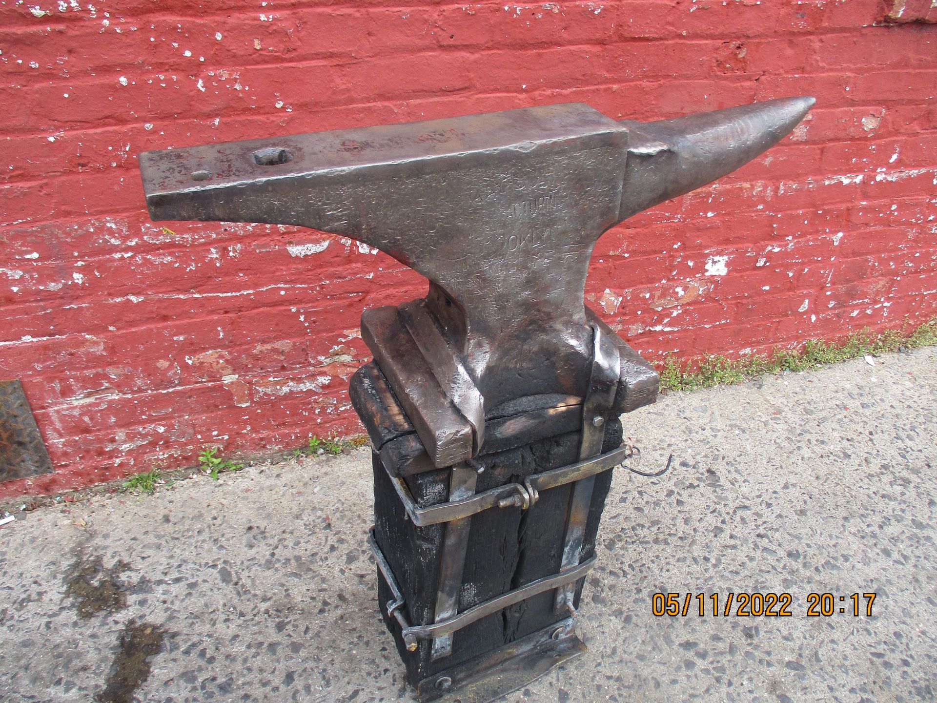 An anvil is sitting in front of a red brick wall