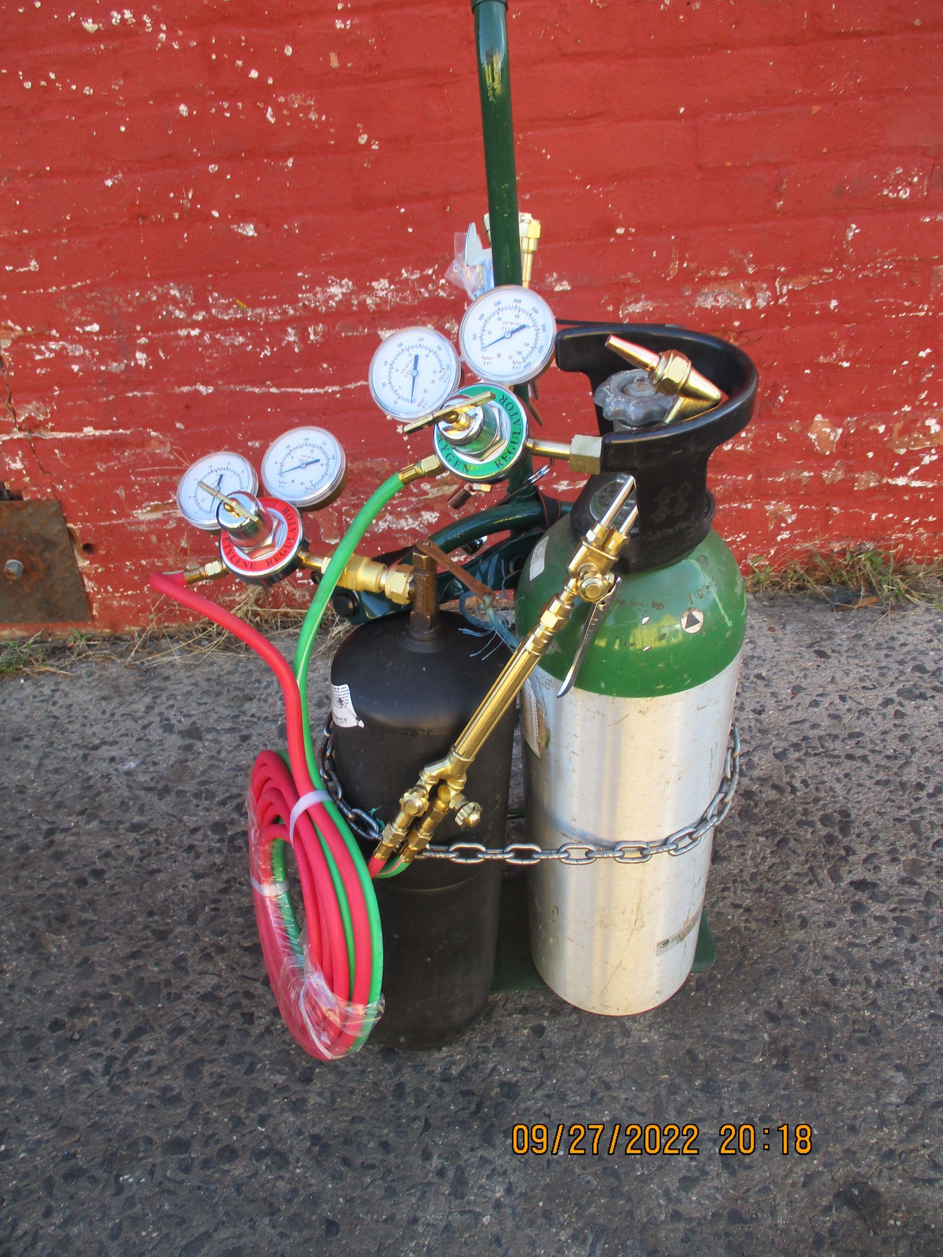 A picture of a propane cylinder with a red brick wall in the background