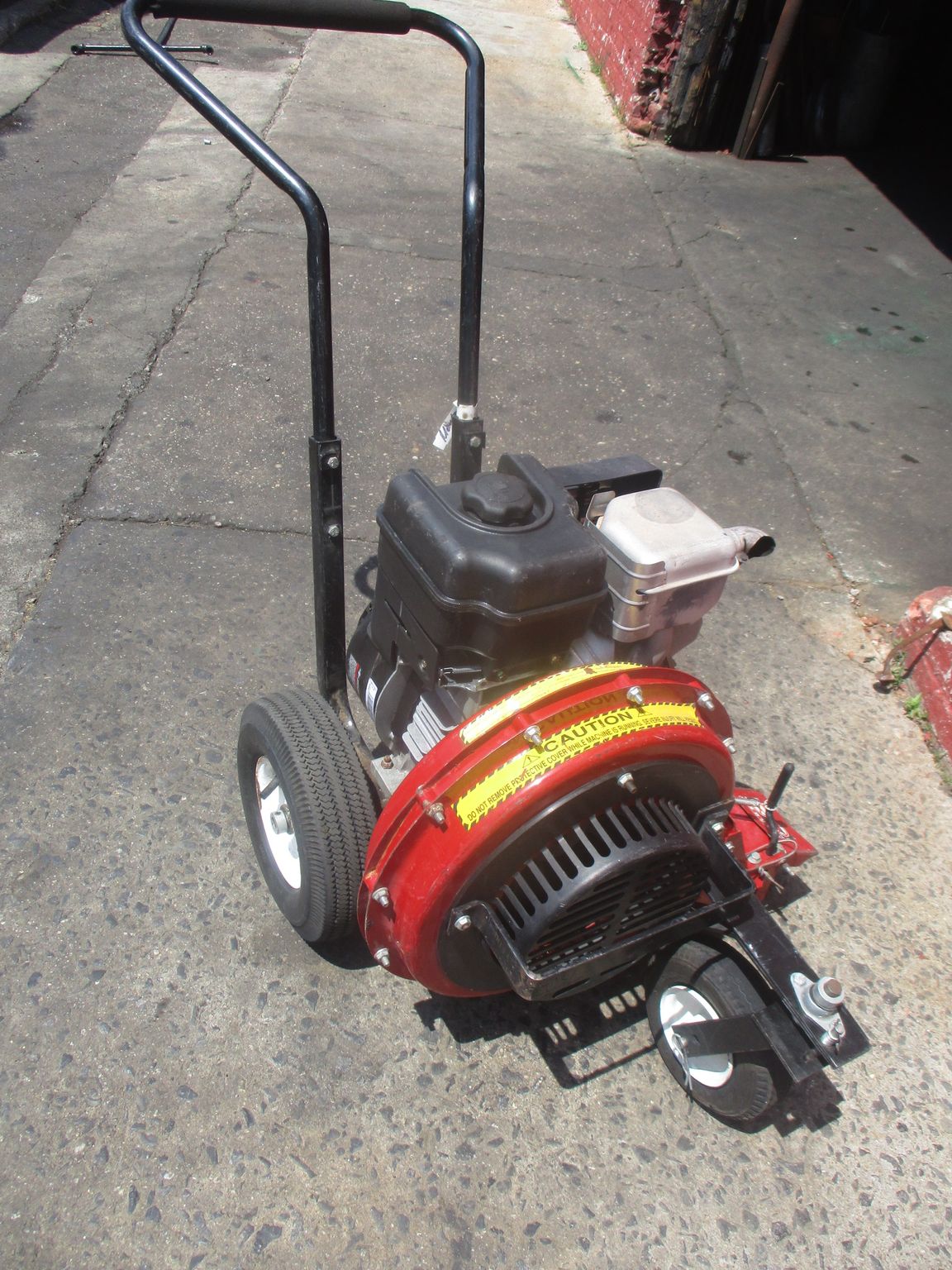A red leaf blower is sitting on the sidewalk
