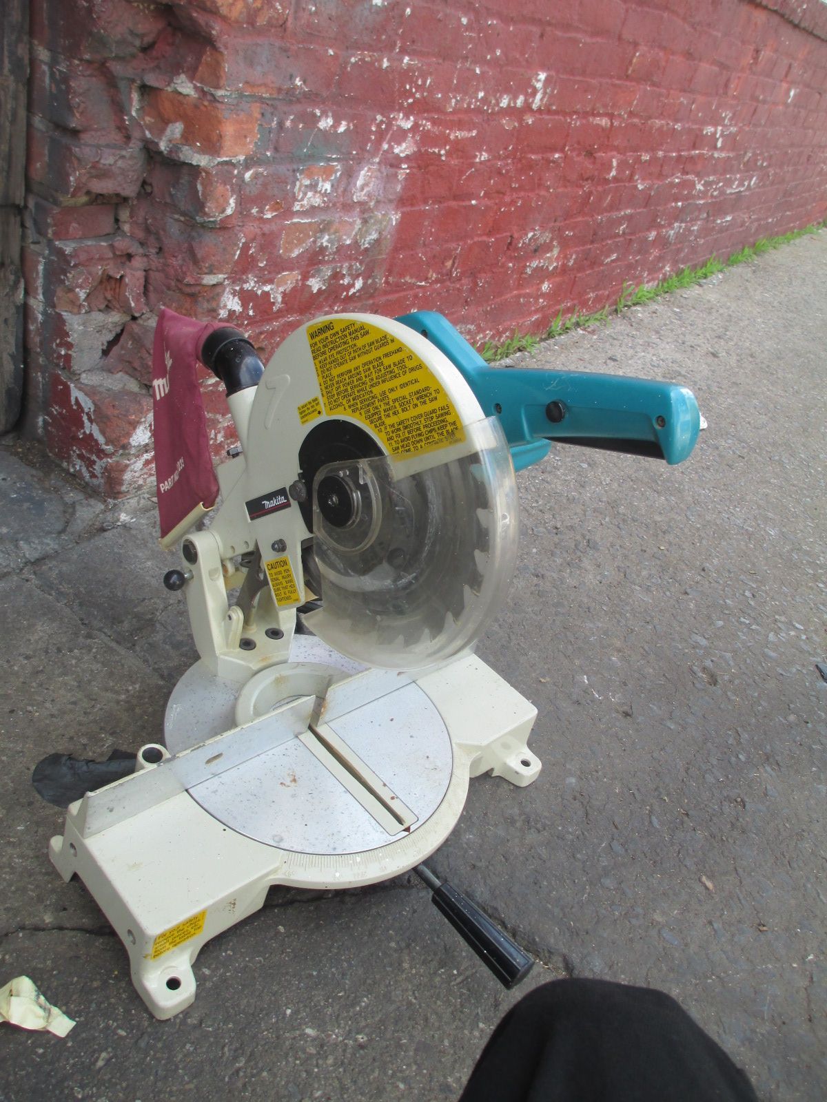 A circular saw is sitting on the ground in front of a brick wall.