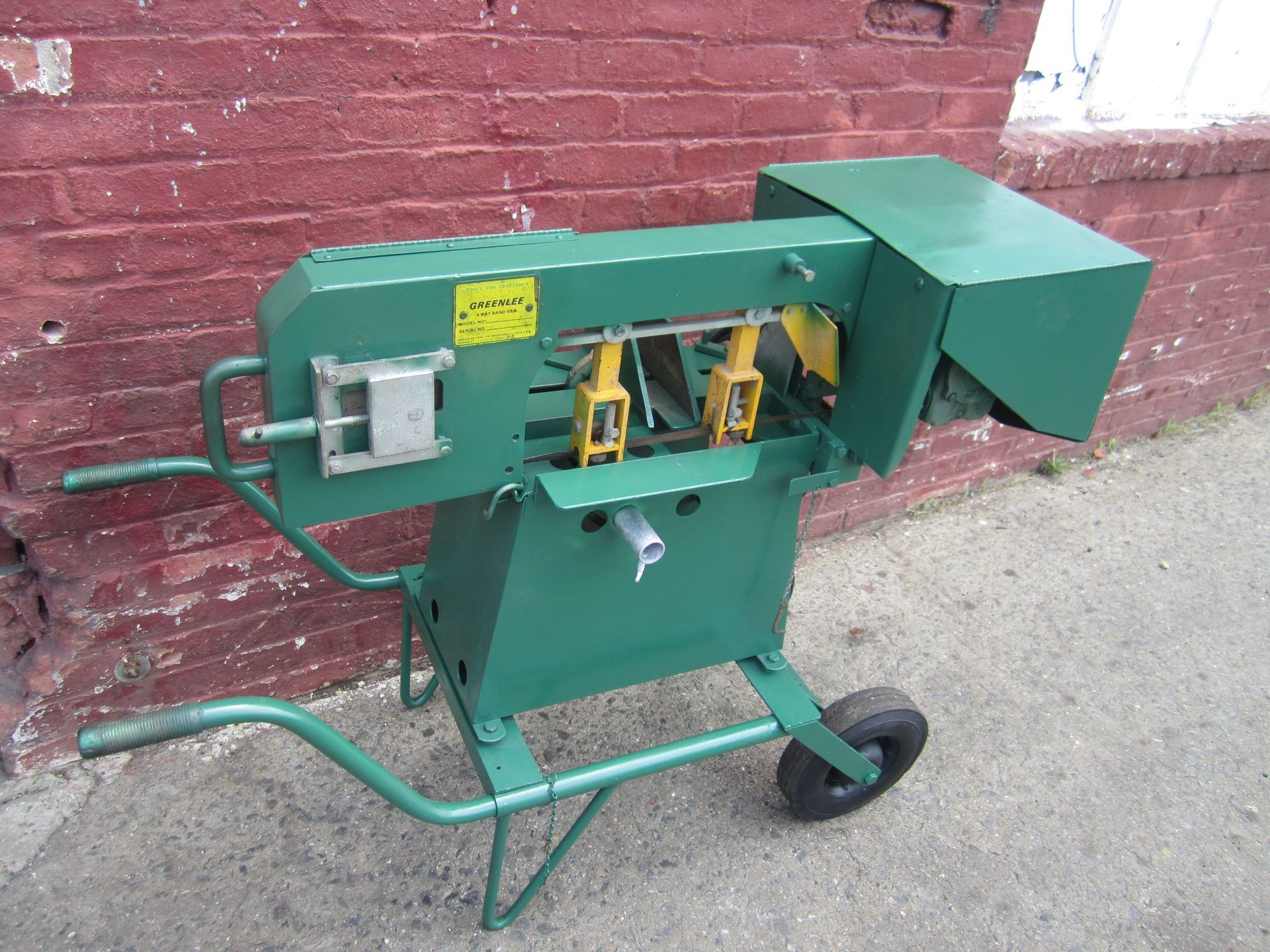 A green machine is sitting on a wheelbarrow in front of a red brick wall