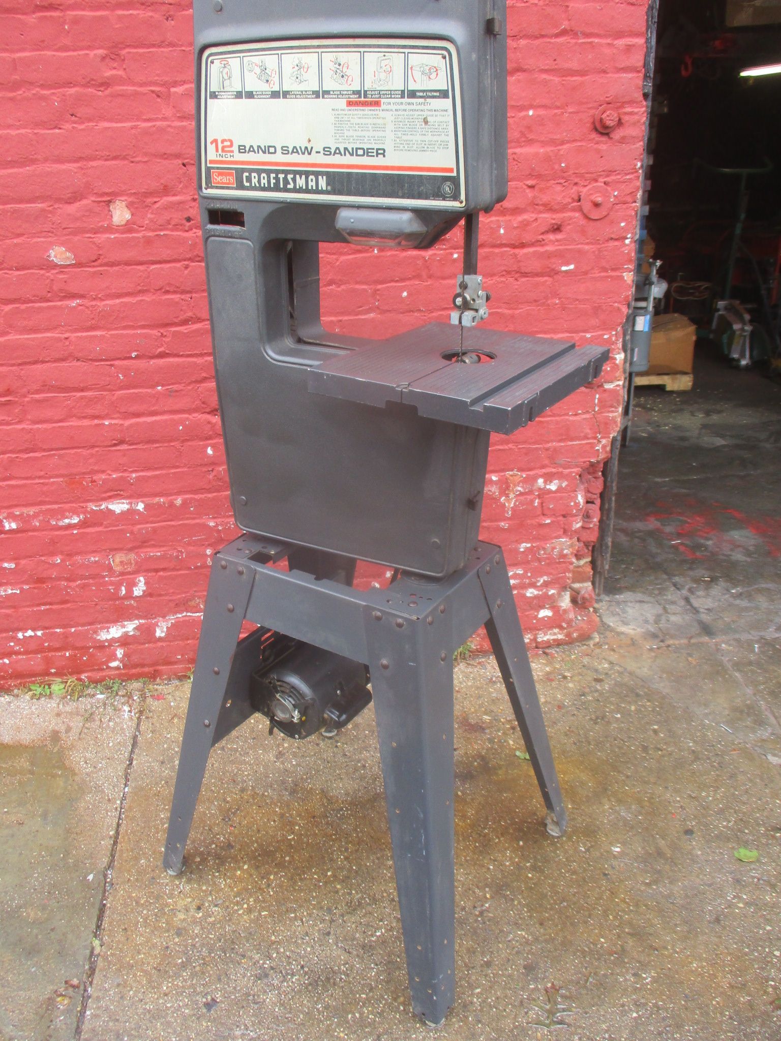 A band saw is sitting in front of a red brick wall
