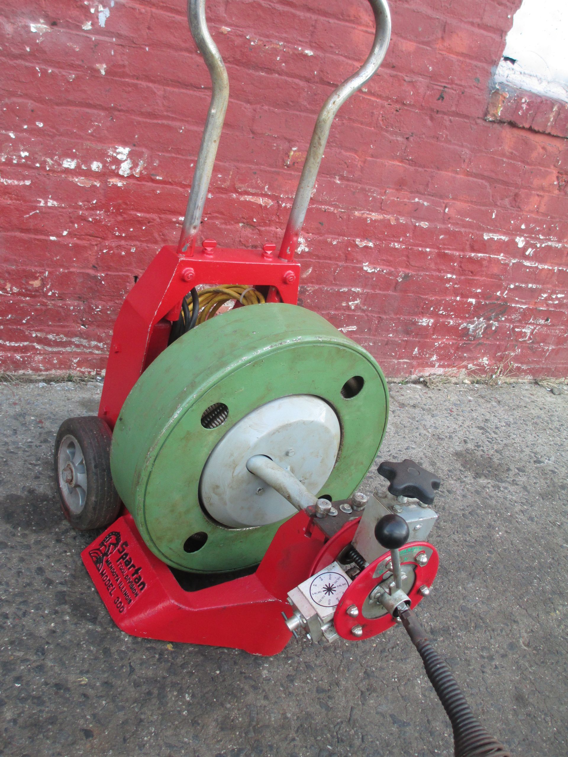 A drain cleaner is sitting on the ground in front of a red brick wall