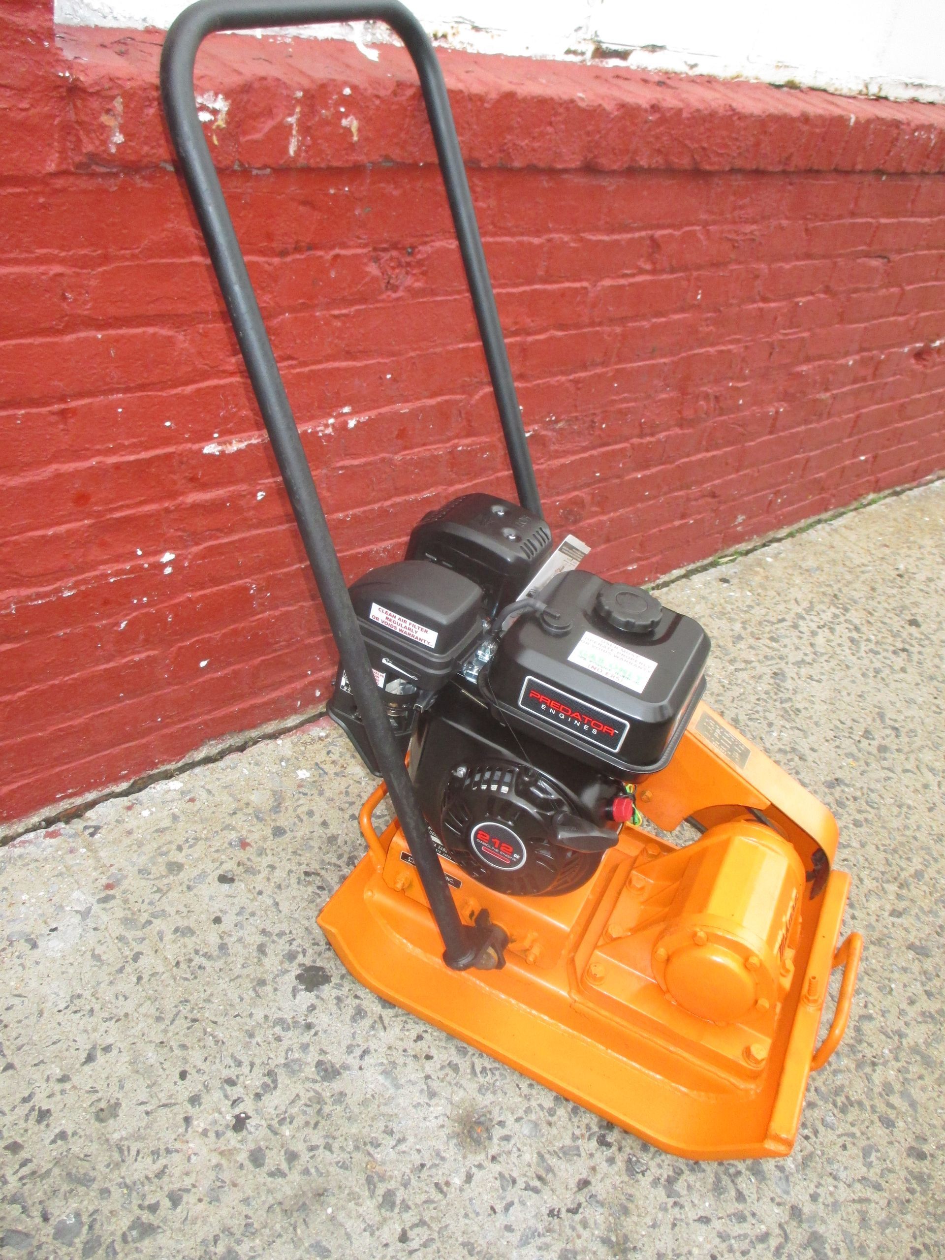 A lawn mower is sitting on the sidewalk in front of a red brick wall