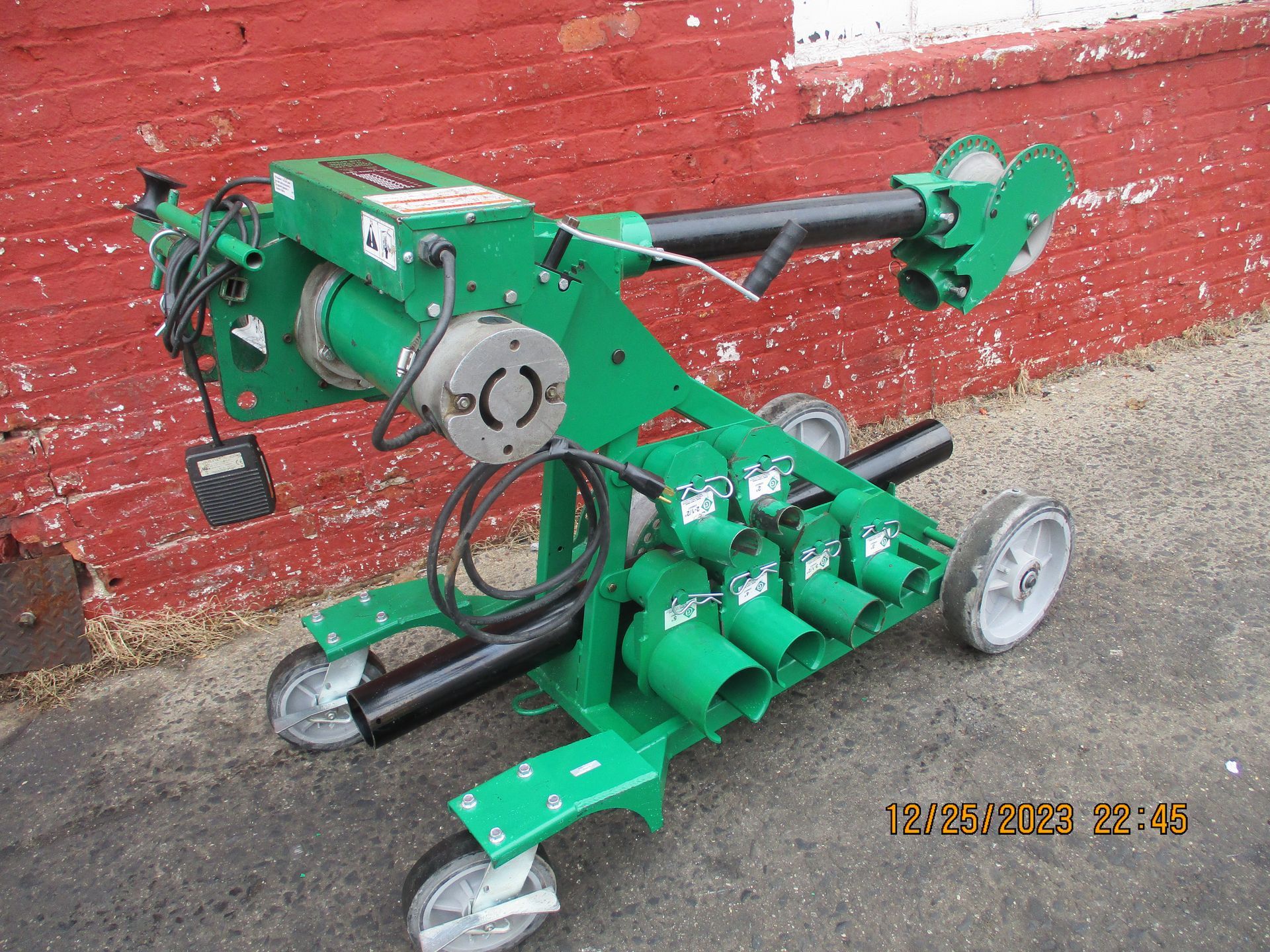 A green machine is sitting in front of a red brick wall