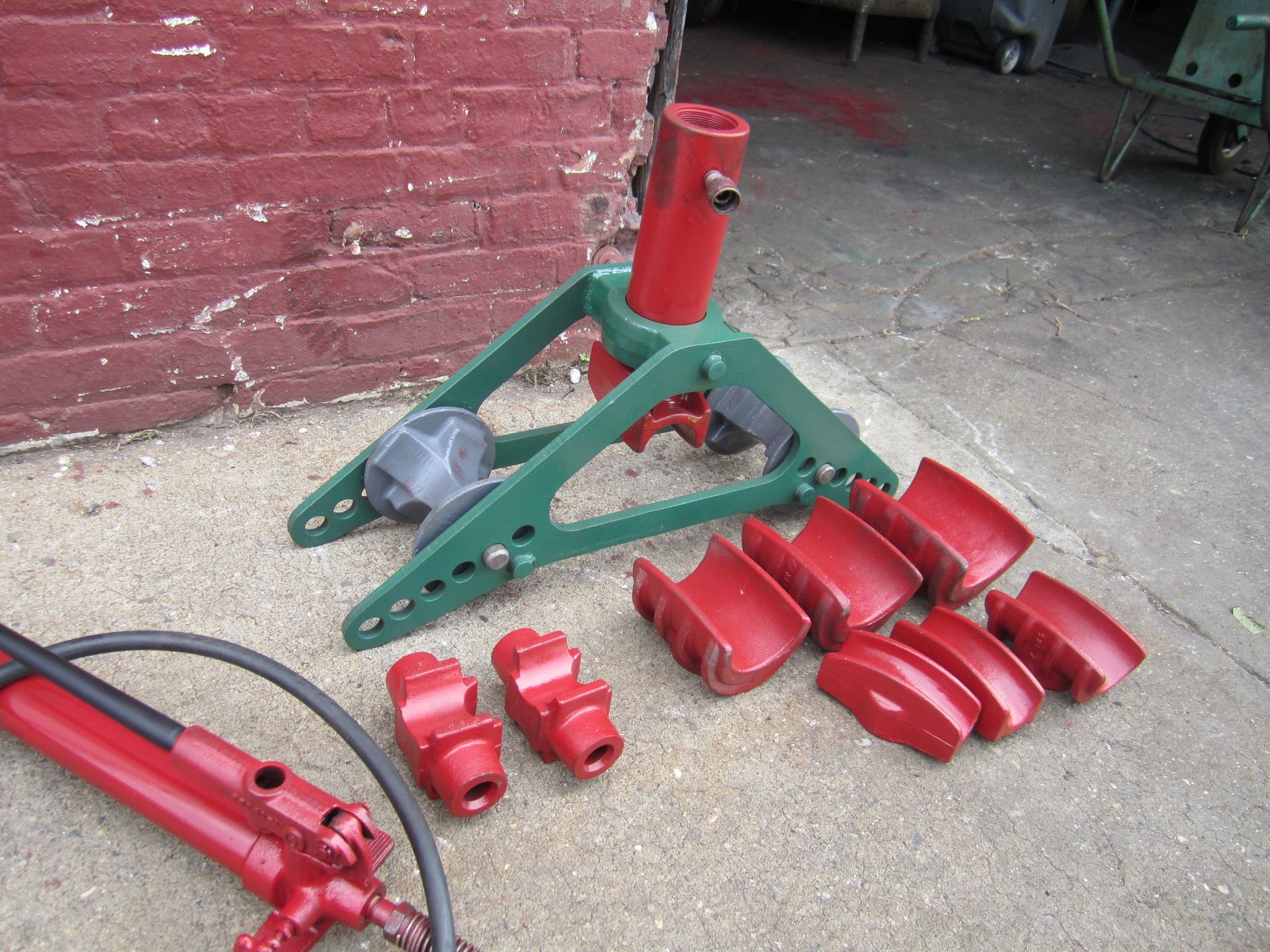 A red and green pipe bending machine is sitting on the ground