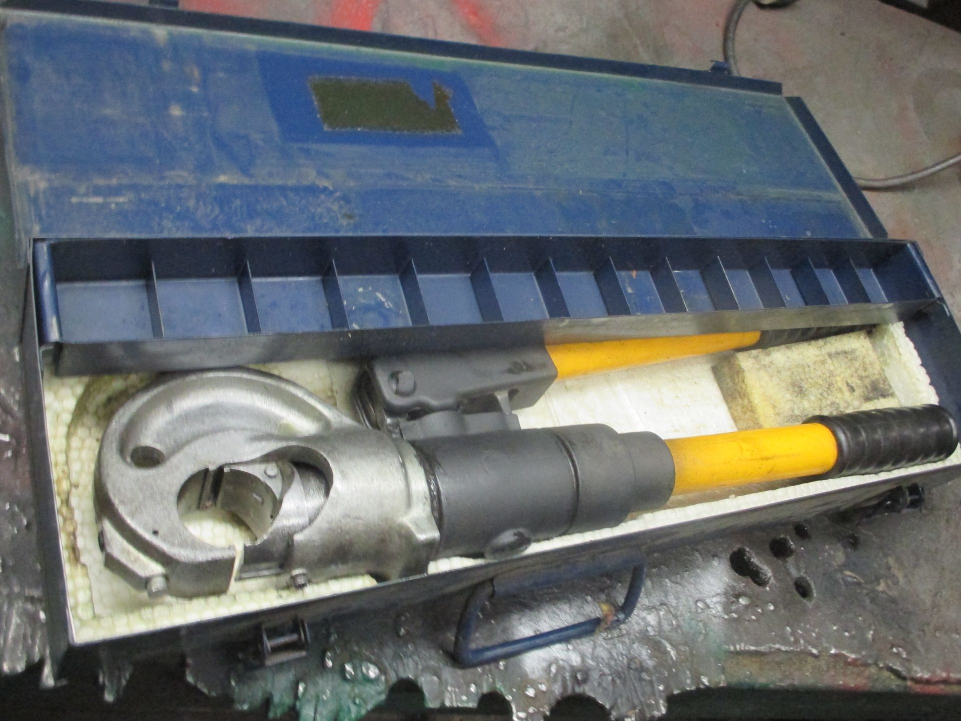 A hydraulic crimping tool is in a case on a table