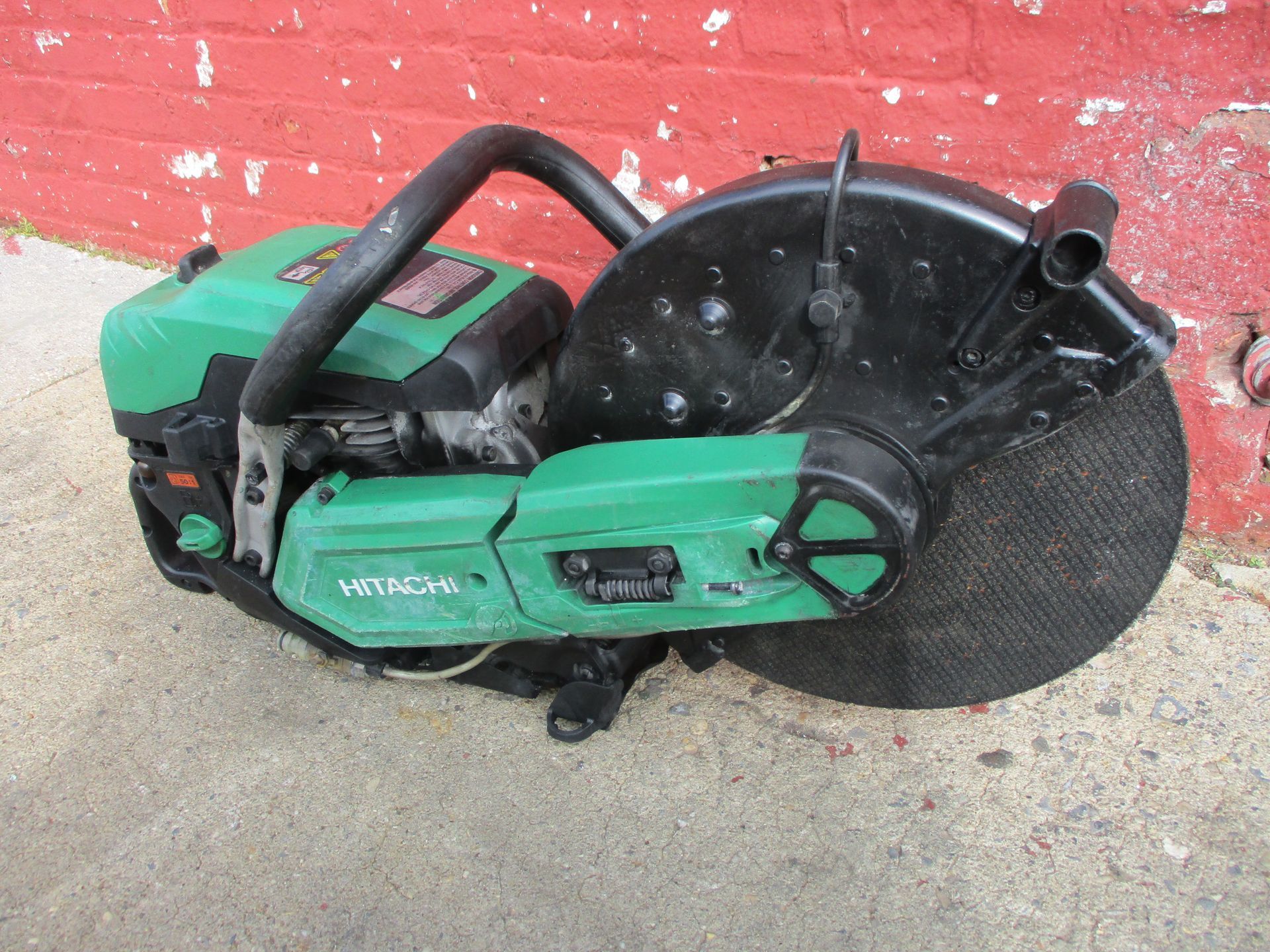 A green and black saw is sitting in front of a red brick wall