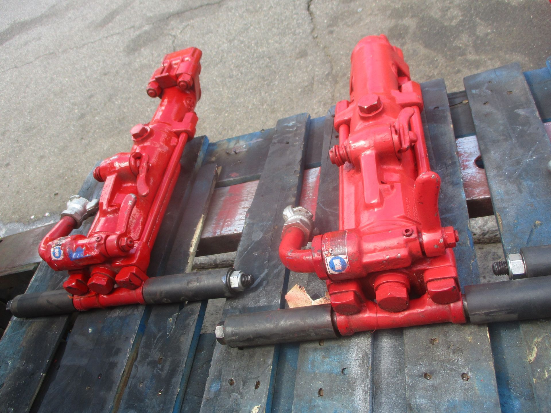 Two red hydraulic drills are sitting on a wooden pallet