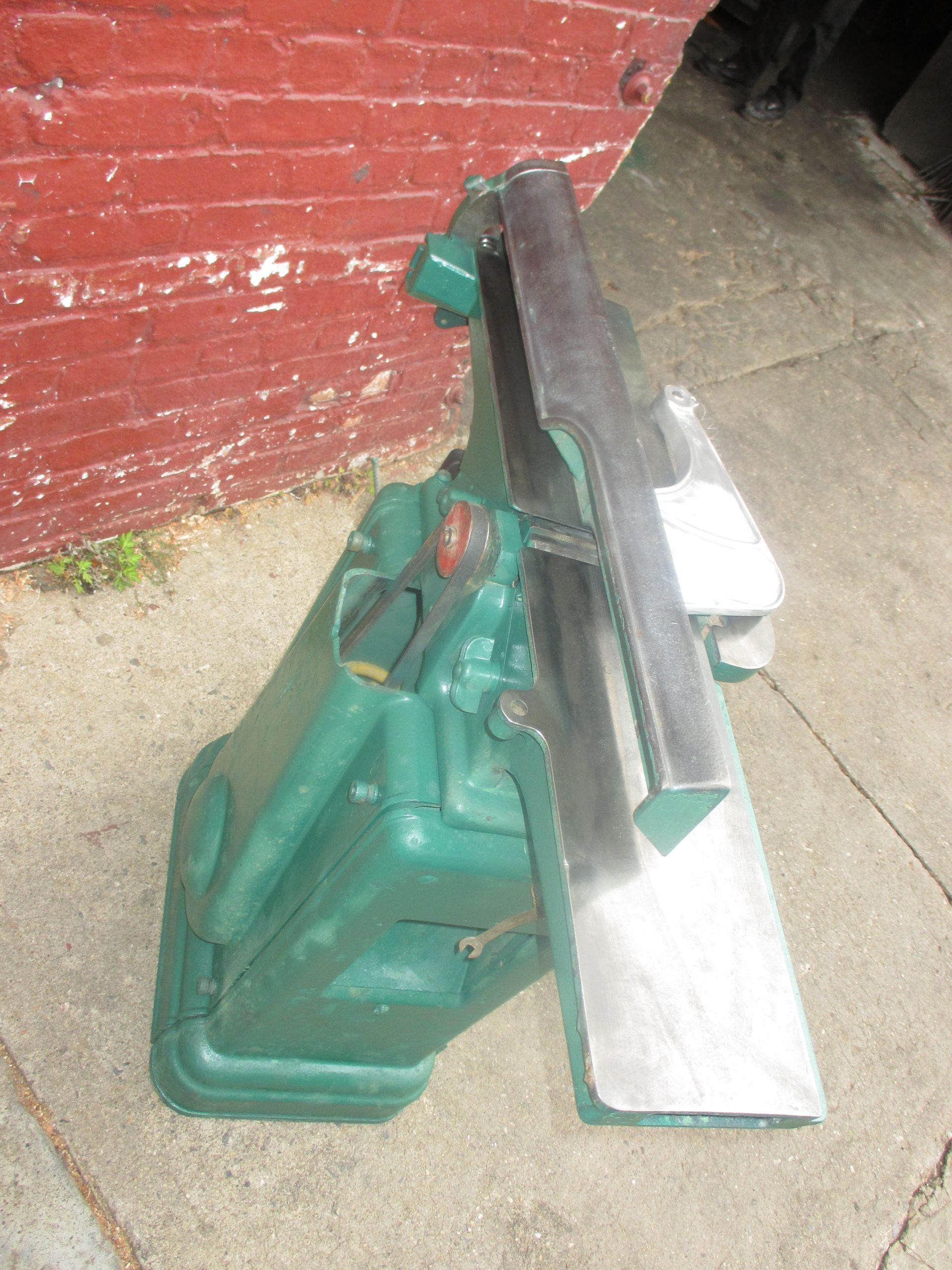 A green machine is sitting in front of a red brick wall