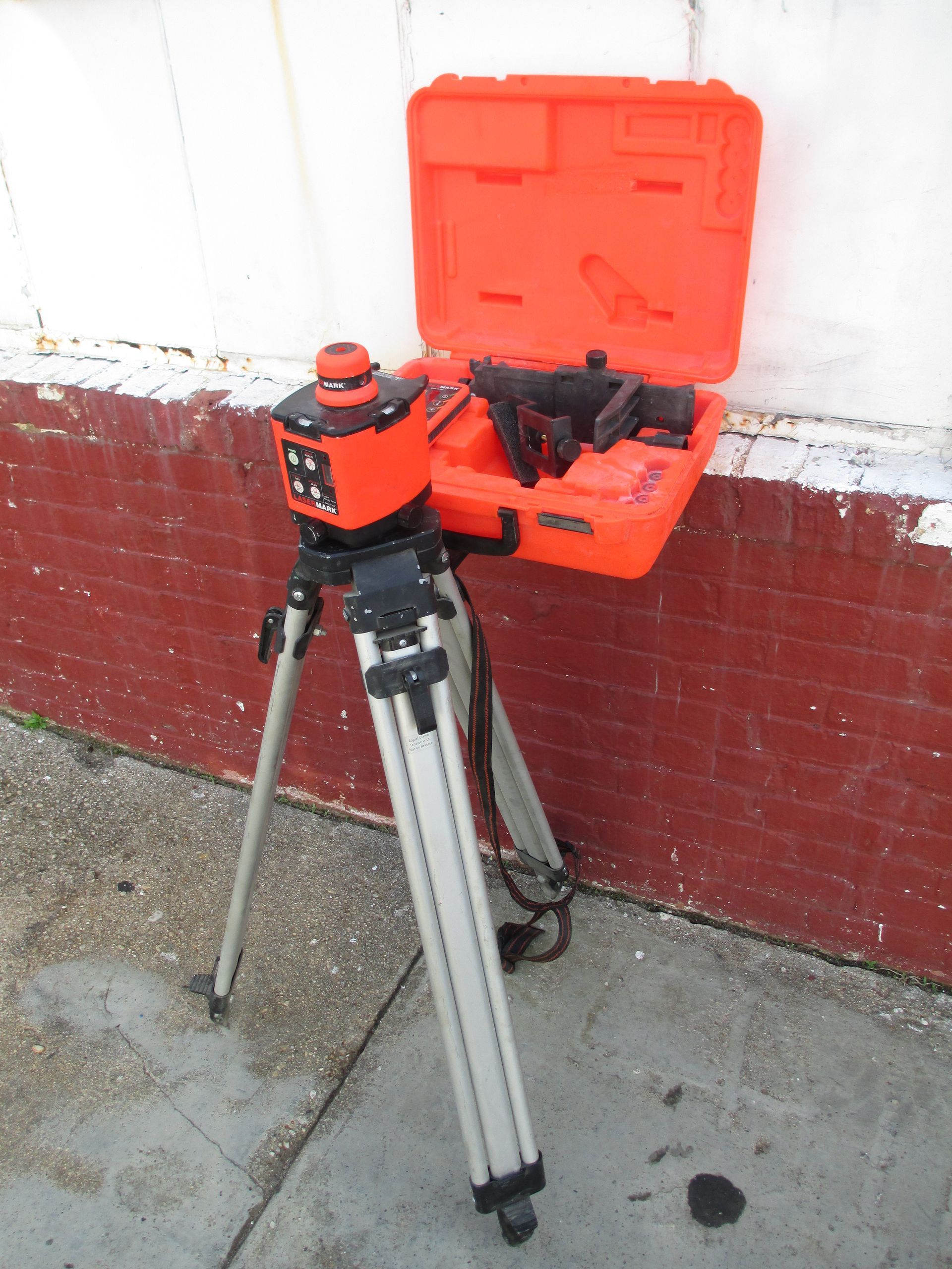 An orange box sits on top of a tripod on a sidewalk