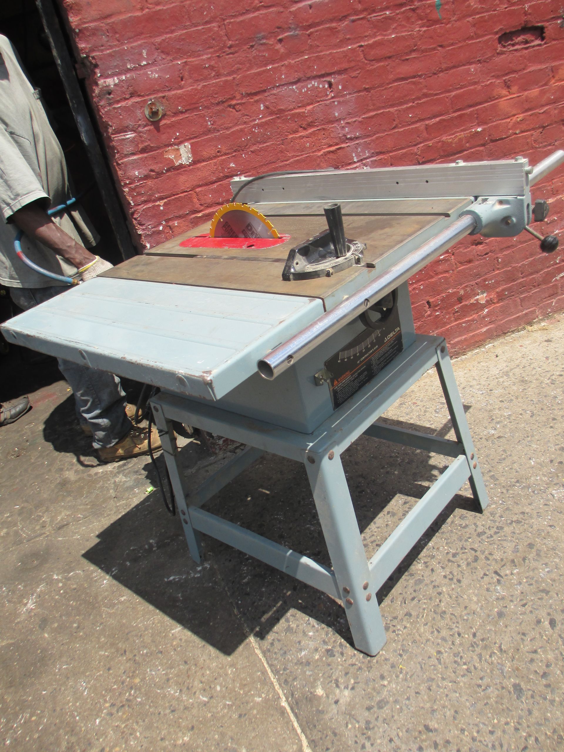 A table saw is sitting in front of a red brick wall