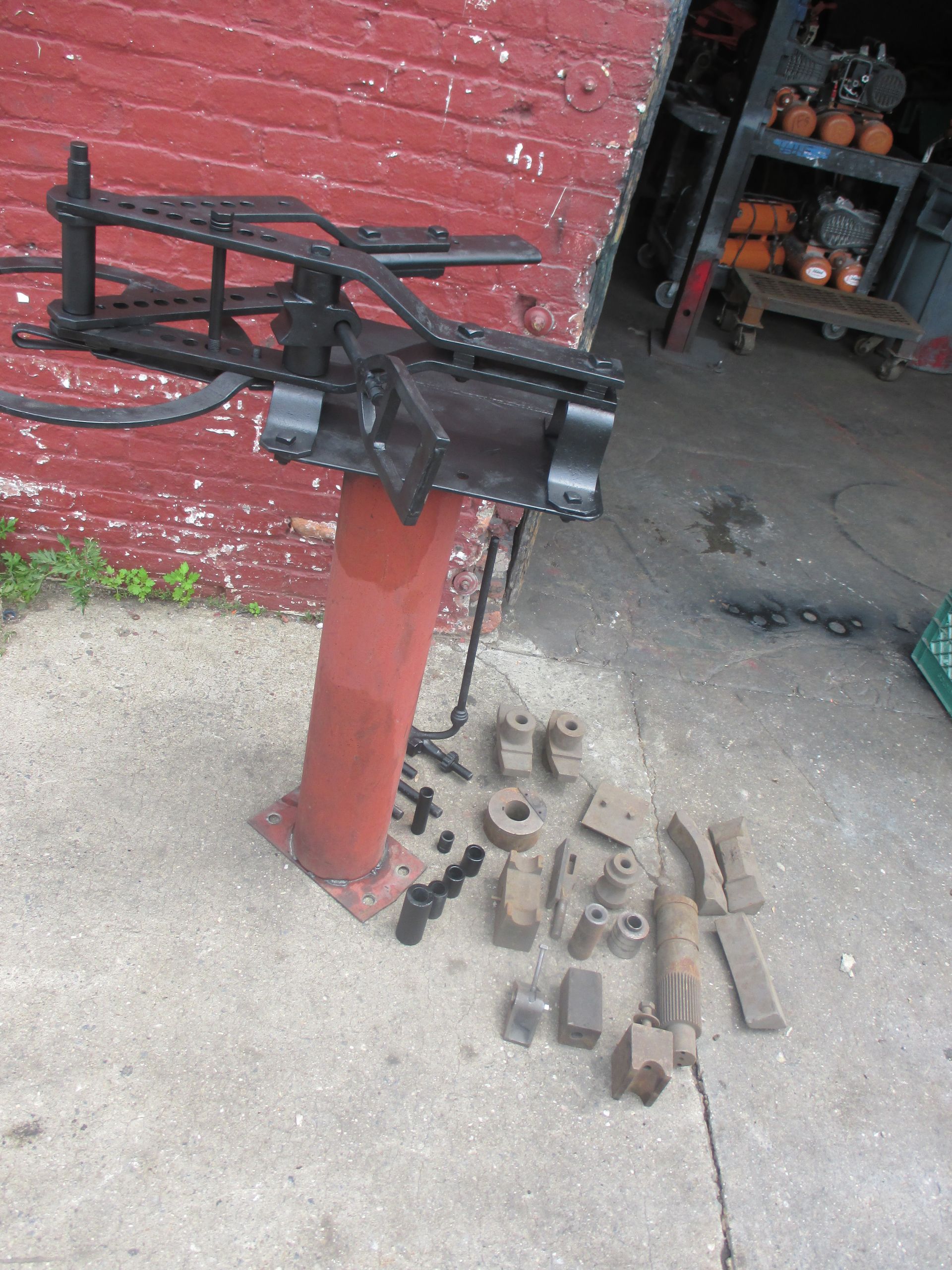 A metal pipe bending machine is sitting on the sidewalk in front of a red brick building