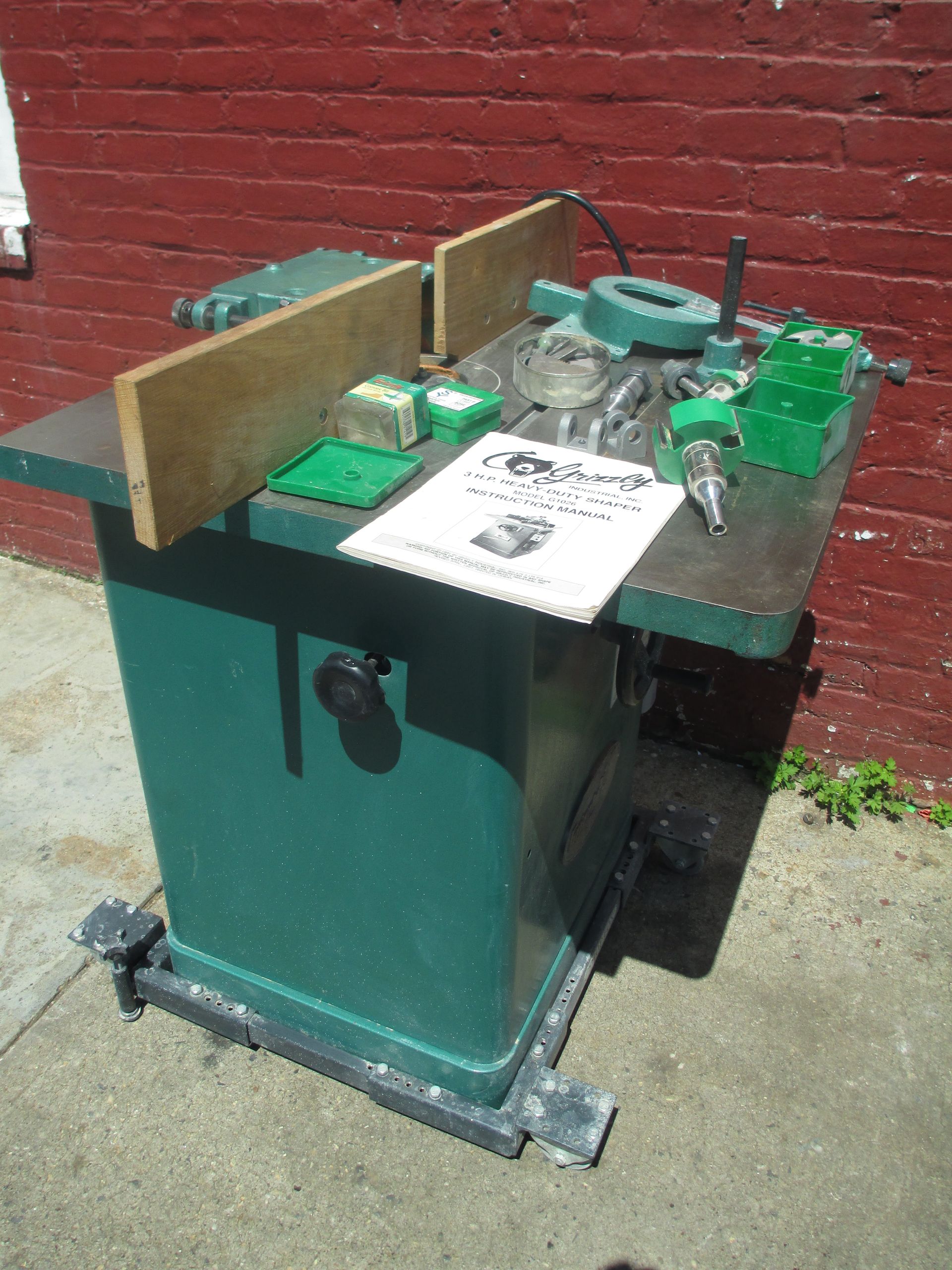 A green machine is sitting in front of a red brick wall