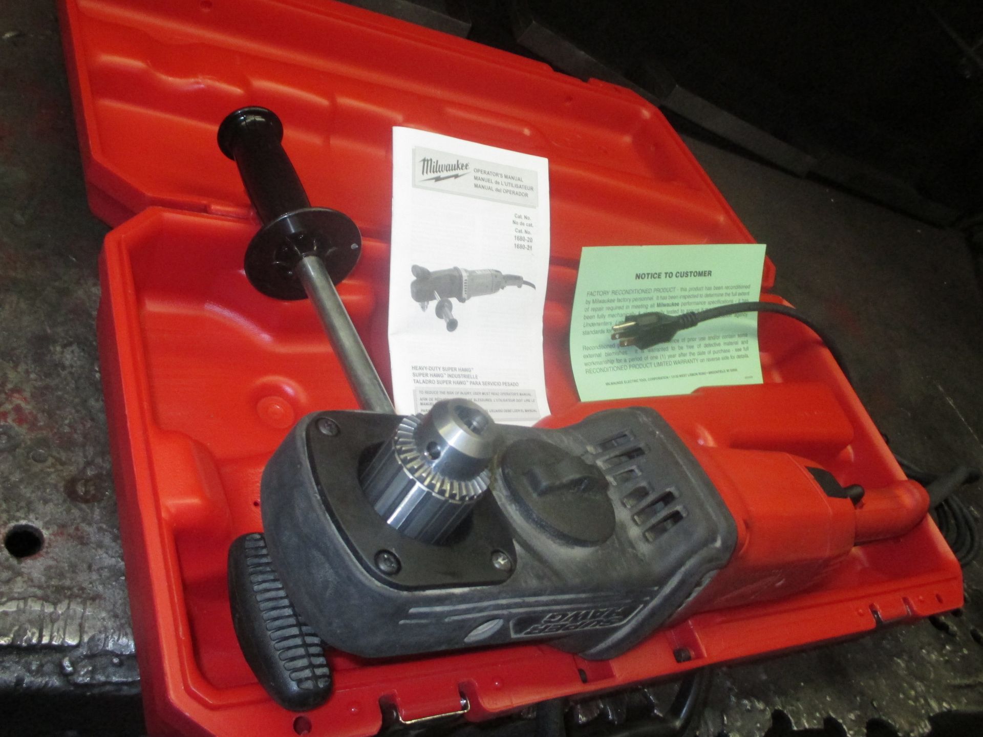 A drill is in a red case next to a manual