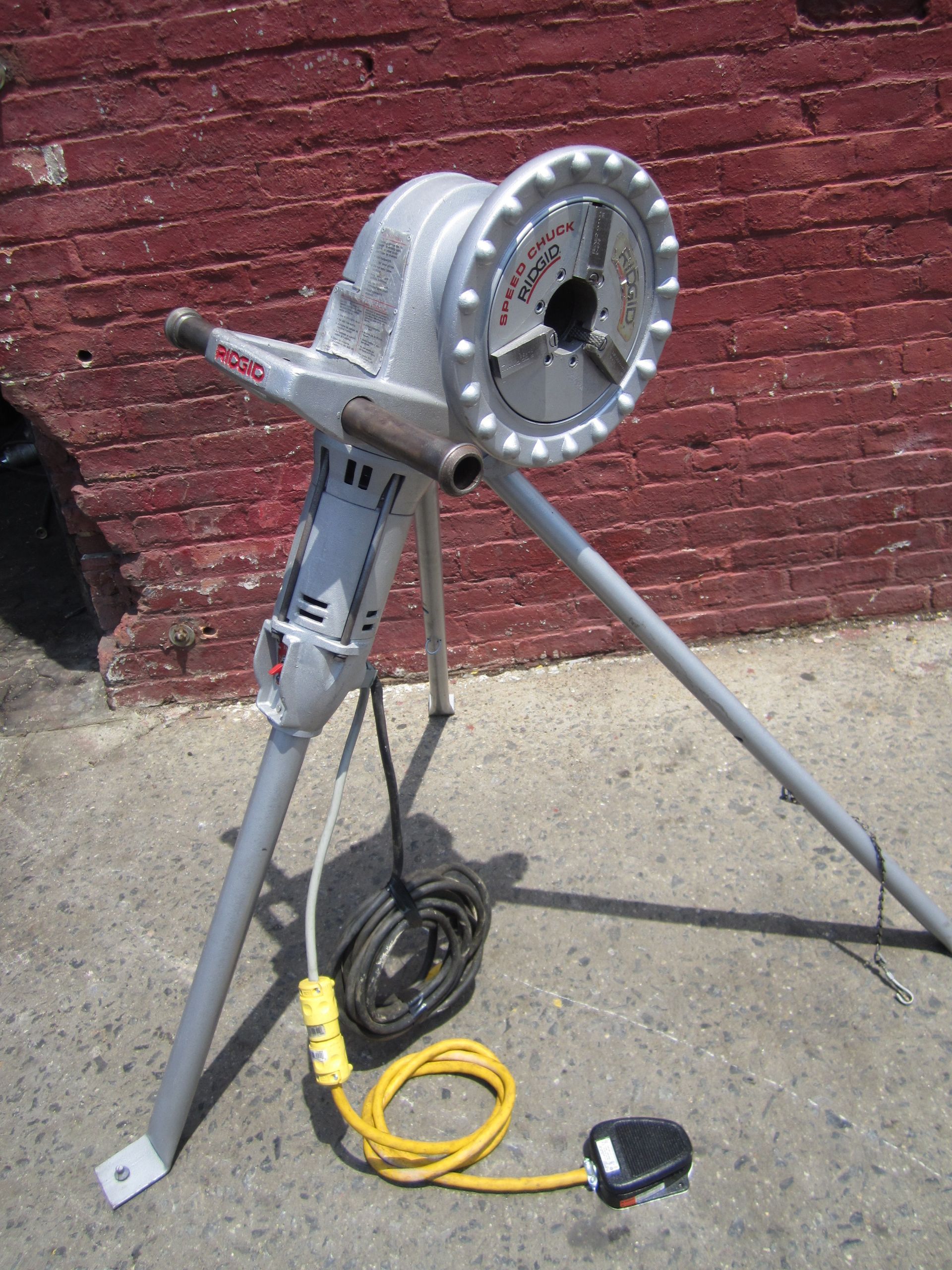 A machine with a yellow cord attached to it is sitting in front of a brick wall