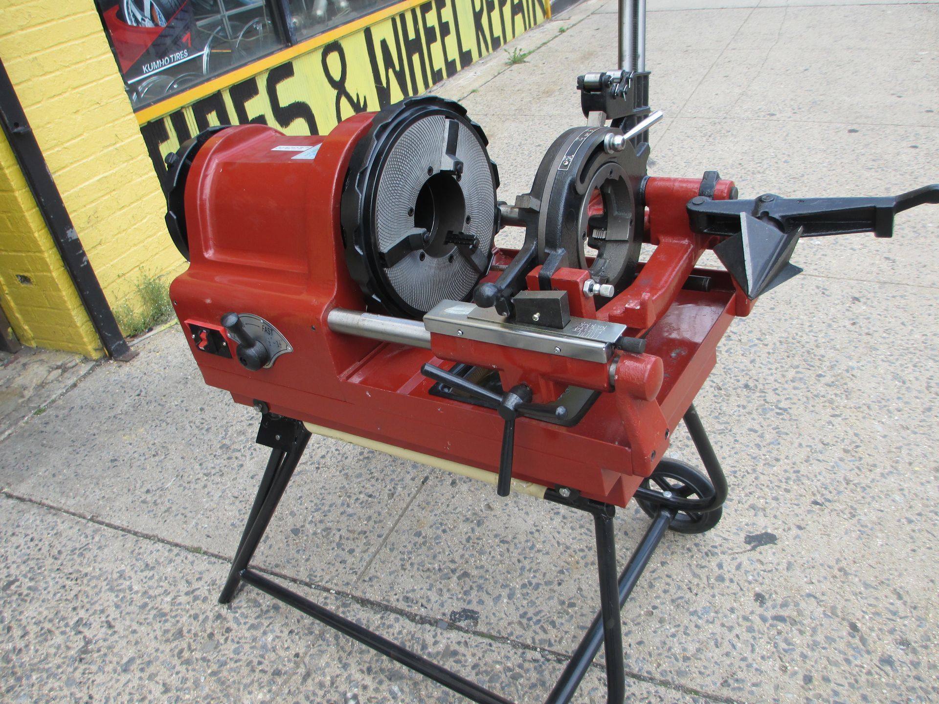 A red machine is sitting on a stand in front of a yellow building.