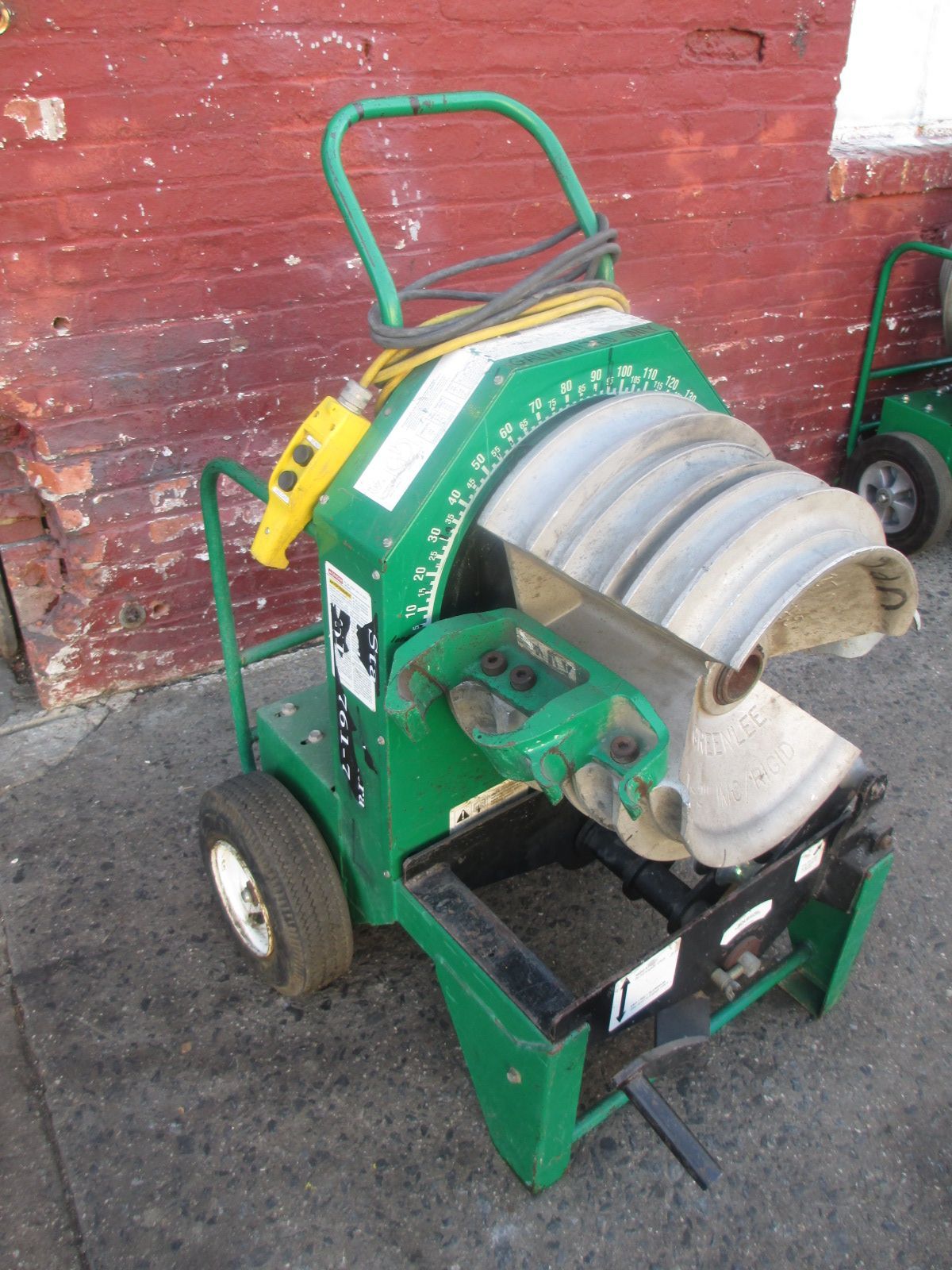 A green machine is sitting in front of a red brick wall