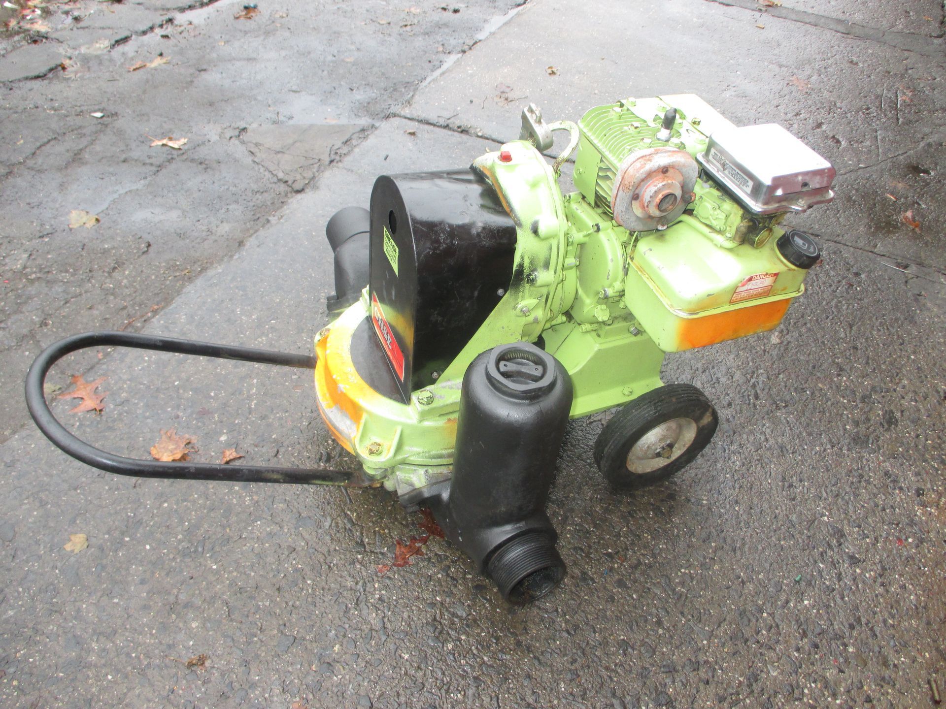 A green and orange lawn mower is parked on the side of the road