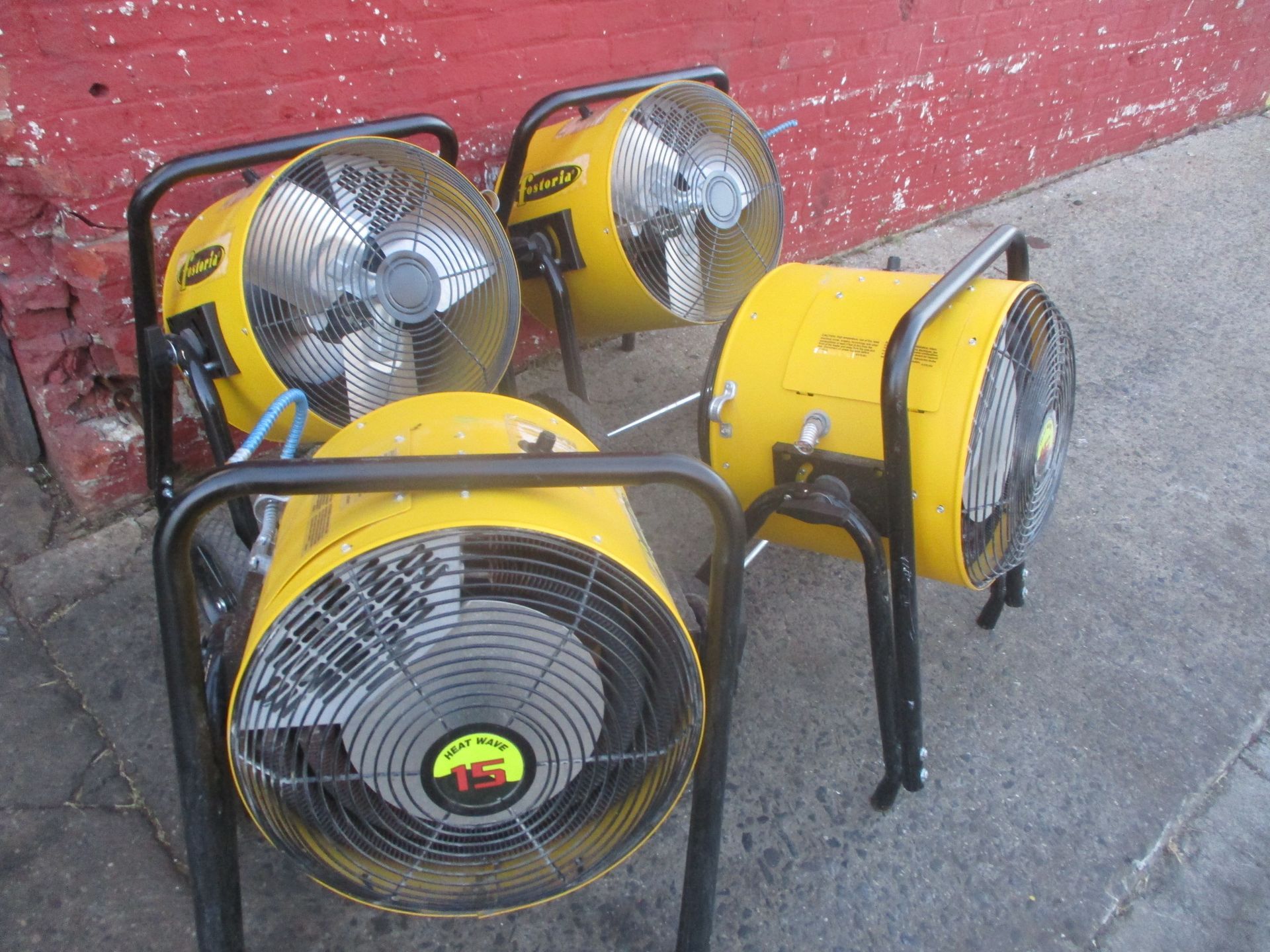 Three yellow fans are sitting on a sidewalk in front of a red brick wall