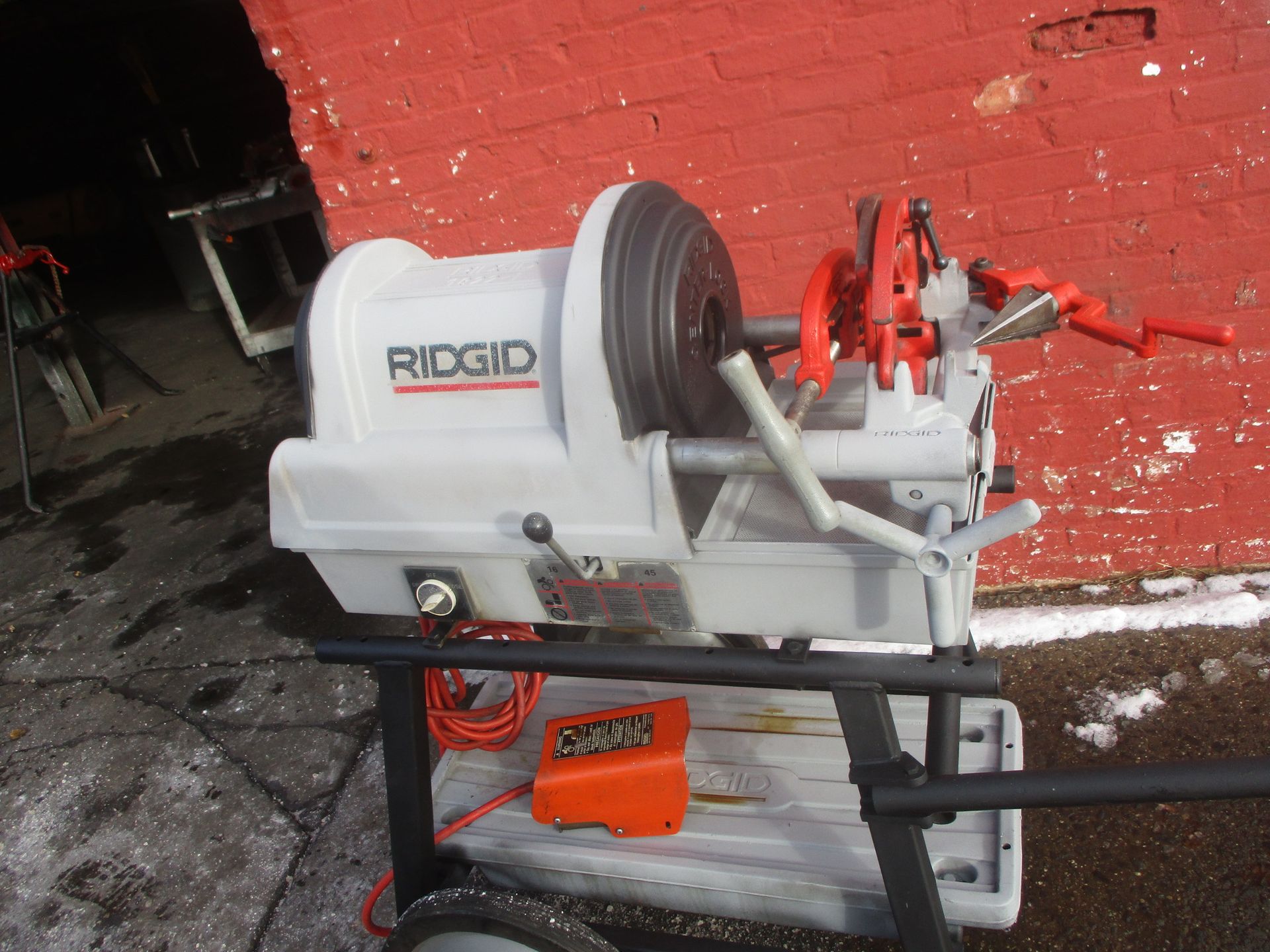 A ridgid machine is sitting on a cart in front of a red brick wall.
