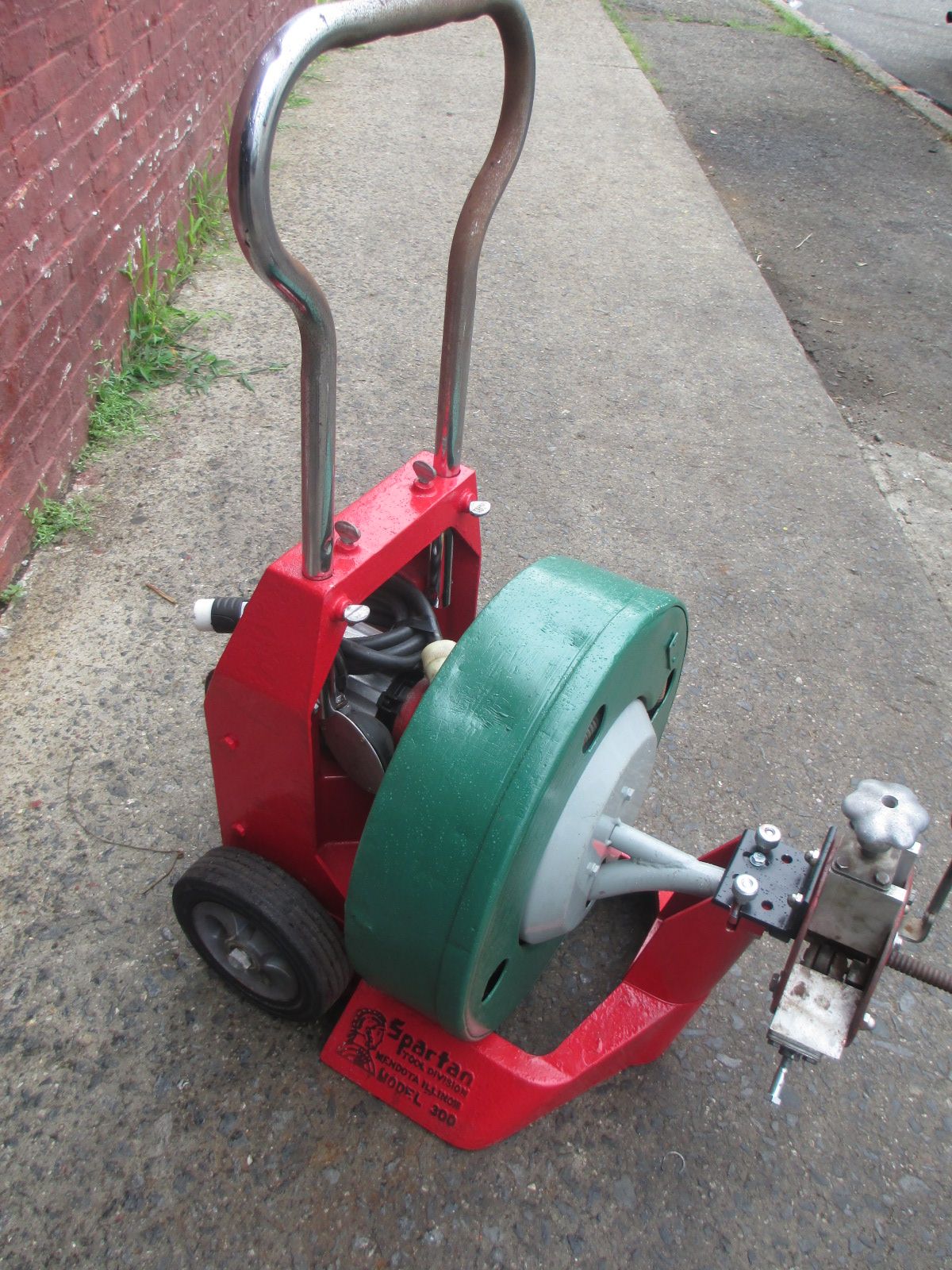 A red and green drain cleaner is sitting on a sidewalk