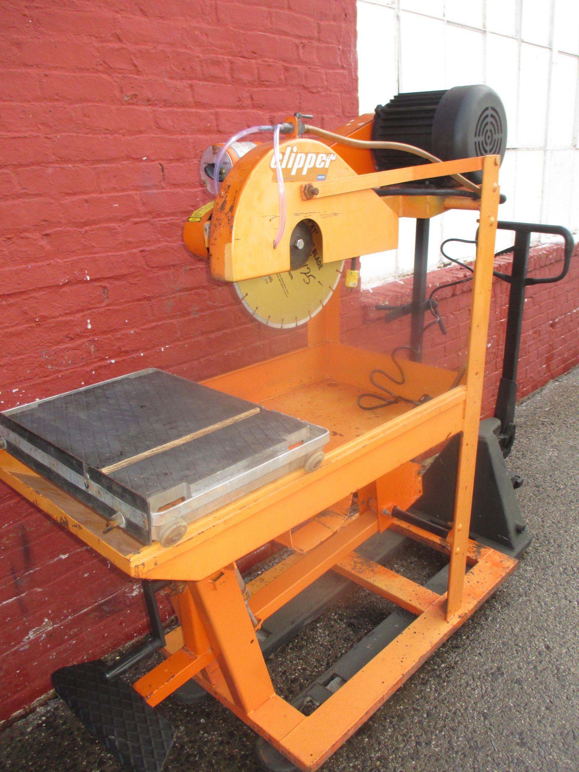 A slipper tile saw is sitting in front of a red brick wall