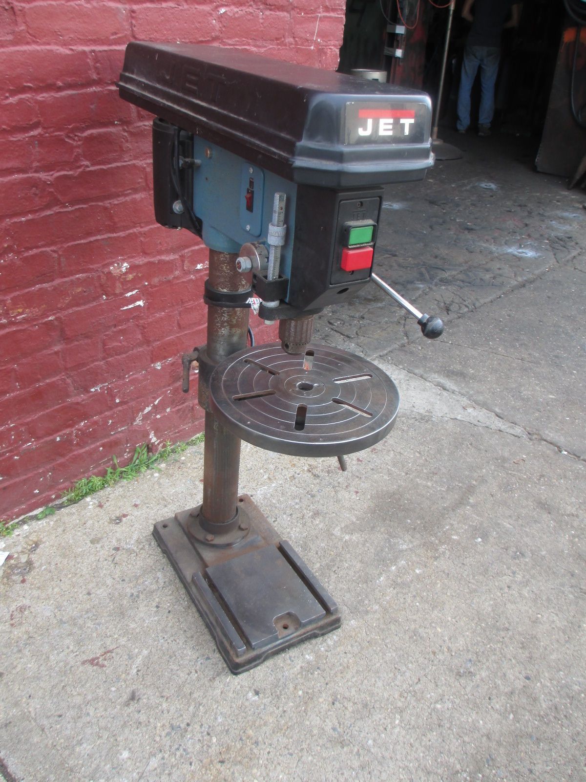 A jet drill is sitting on the sidewalk in front of a red brick wall