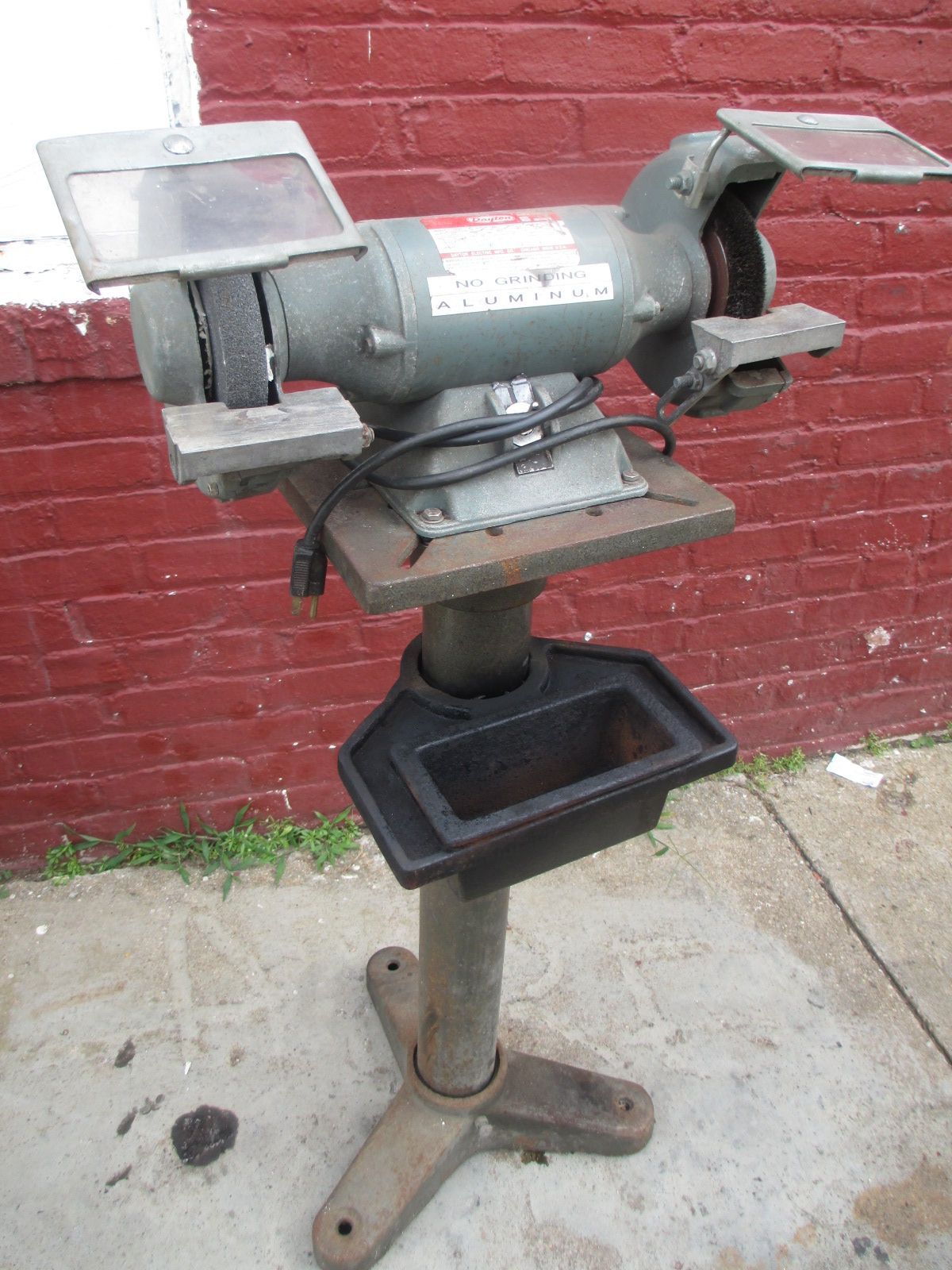 A grinder is sitting on the sidewalk in front of a red brick wall