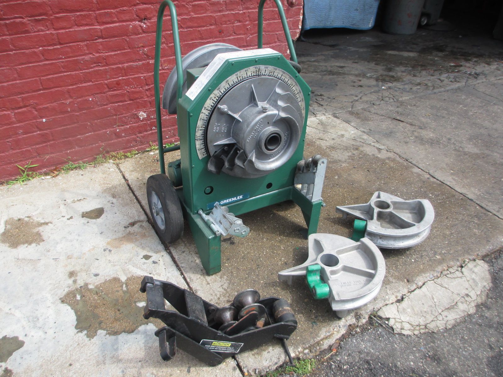 A green pipe bending machine is sitting on the sidewalk