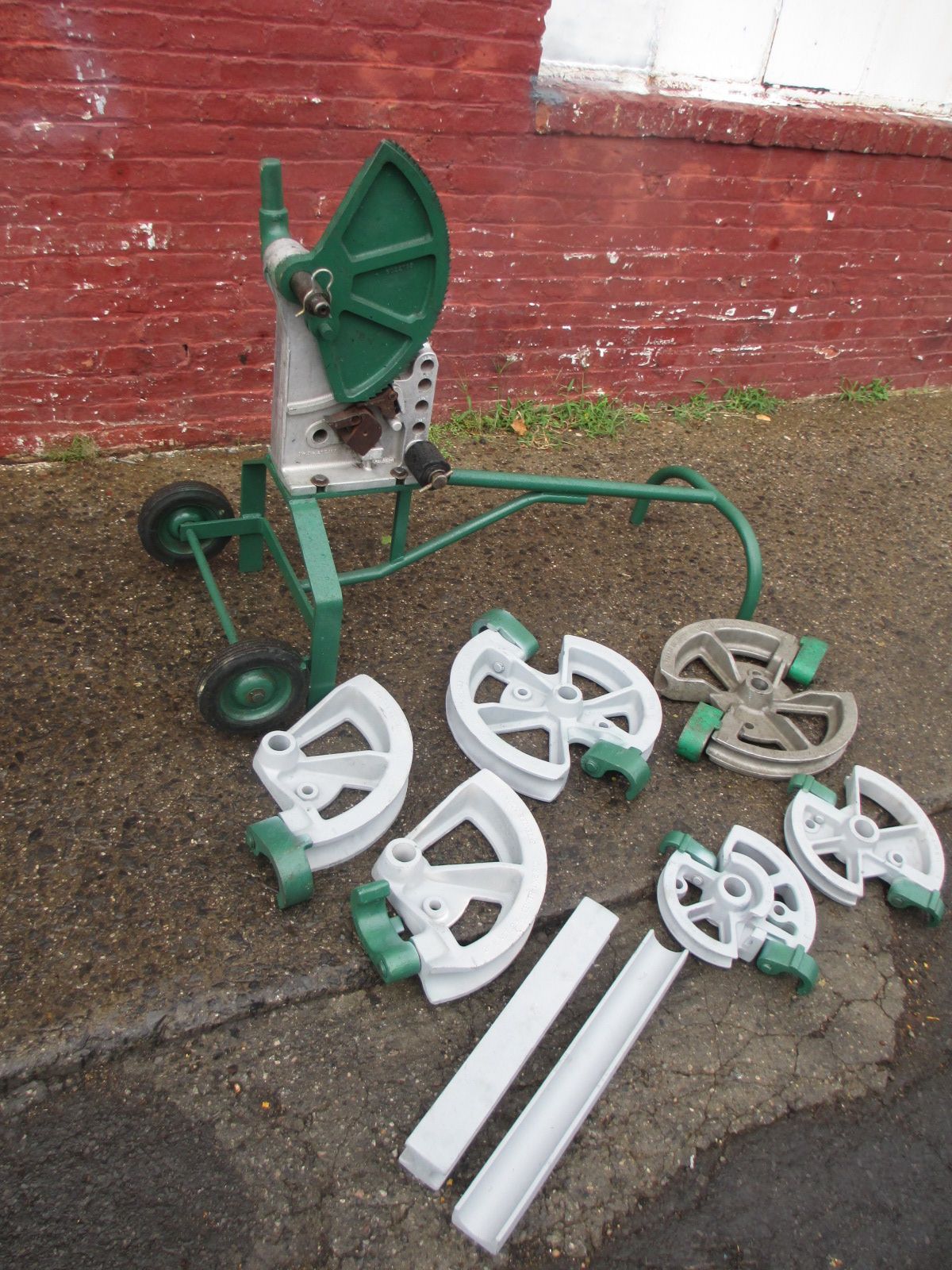 A green and white pipe bending machine is sitting on the sidewalk
