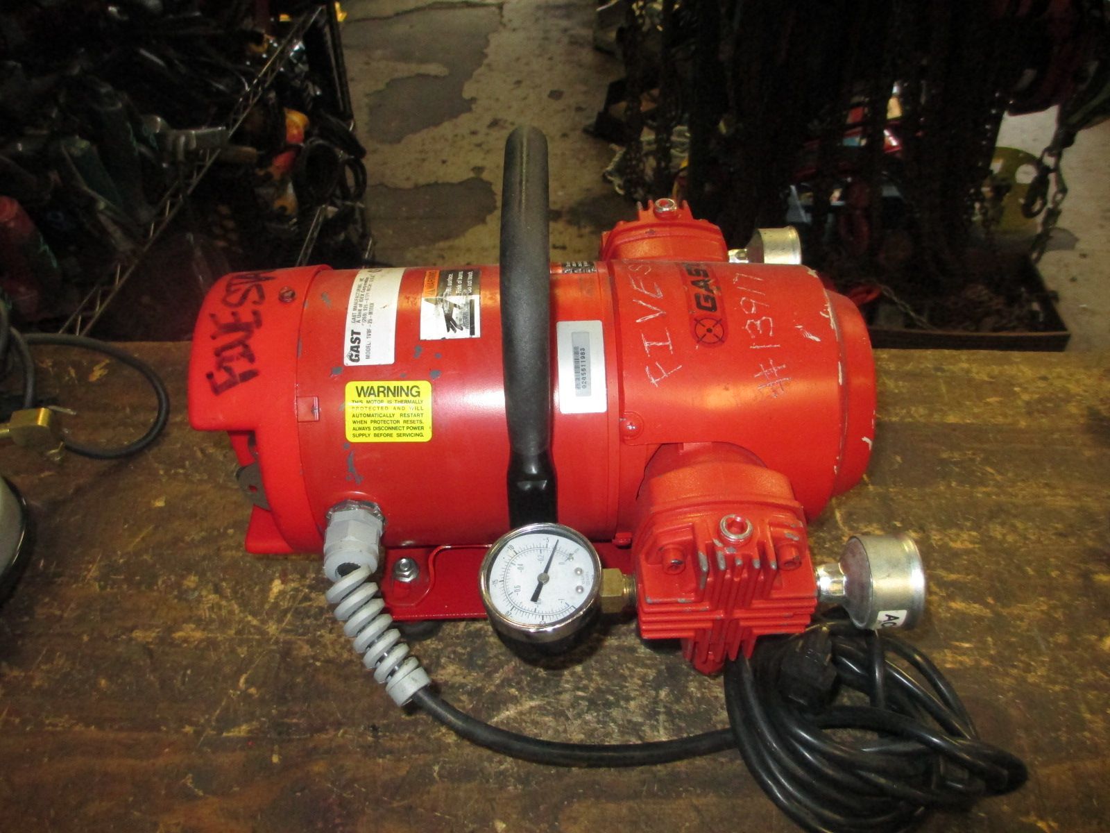 A red pump with a gauge attached to it is sitting on a wooden table.