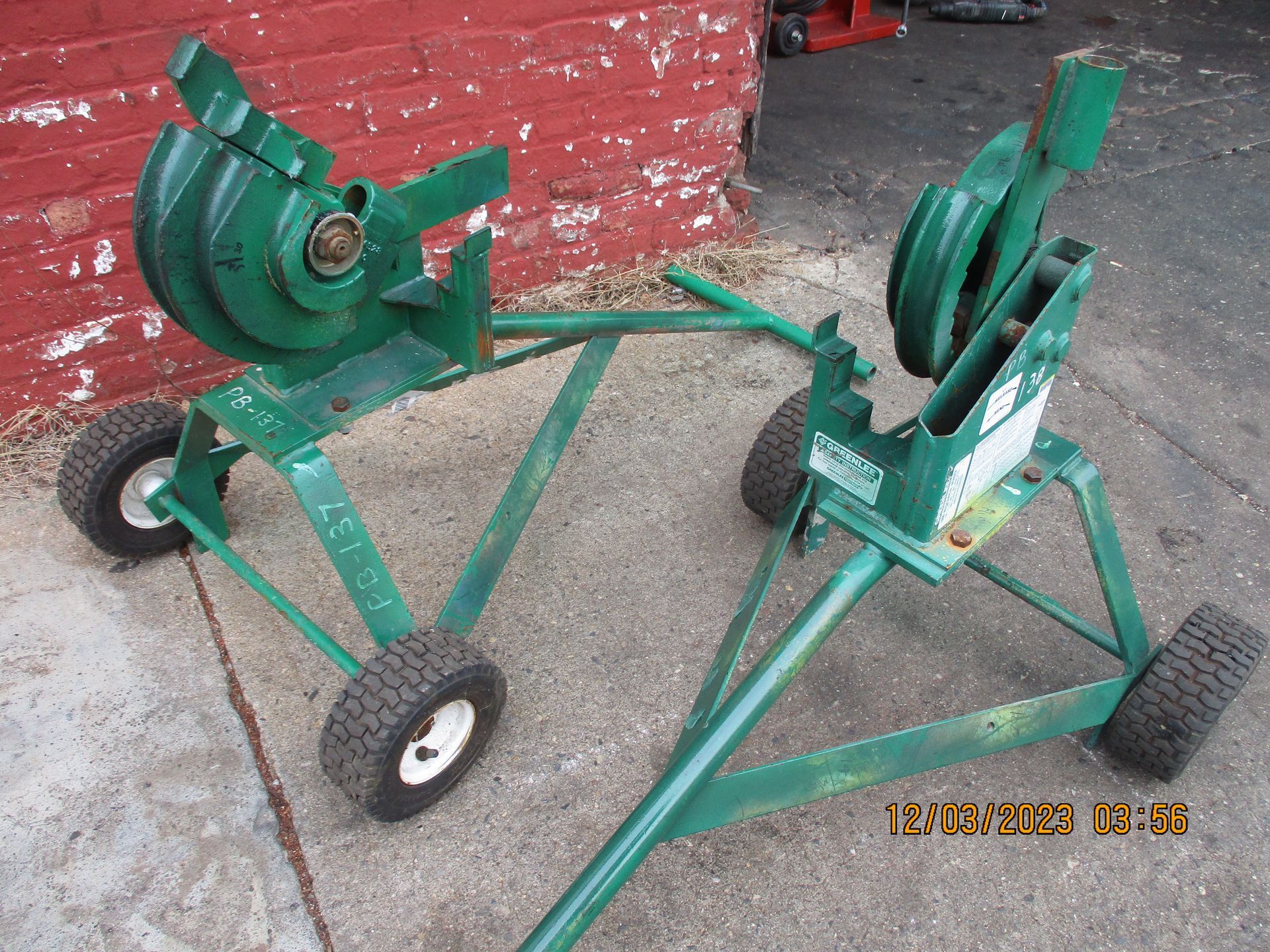 Two green pipe benders are sitting on a sidewalk in front of a red brick wall